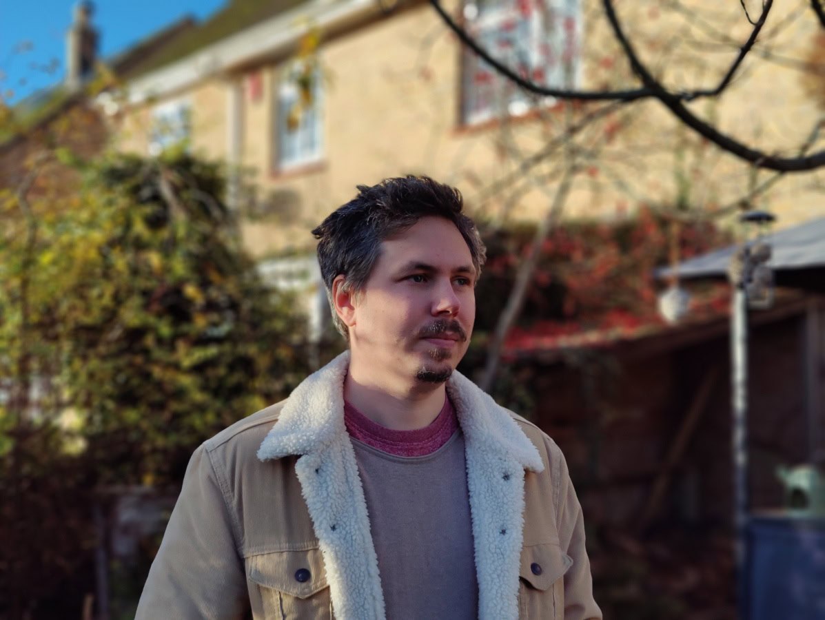 Portrait of man standing outdoors in front of brick house shot on OnePlus 9 Pro