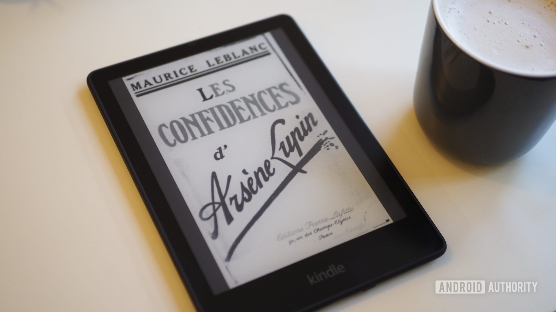 Amazon Kindle Paperwhite 2021 with the surface  showing a publication  cover, connected  a table, adjacent  to a cupful  of coffee