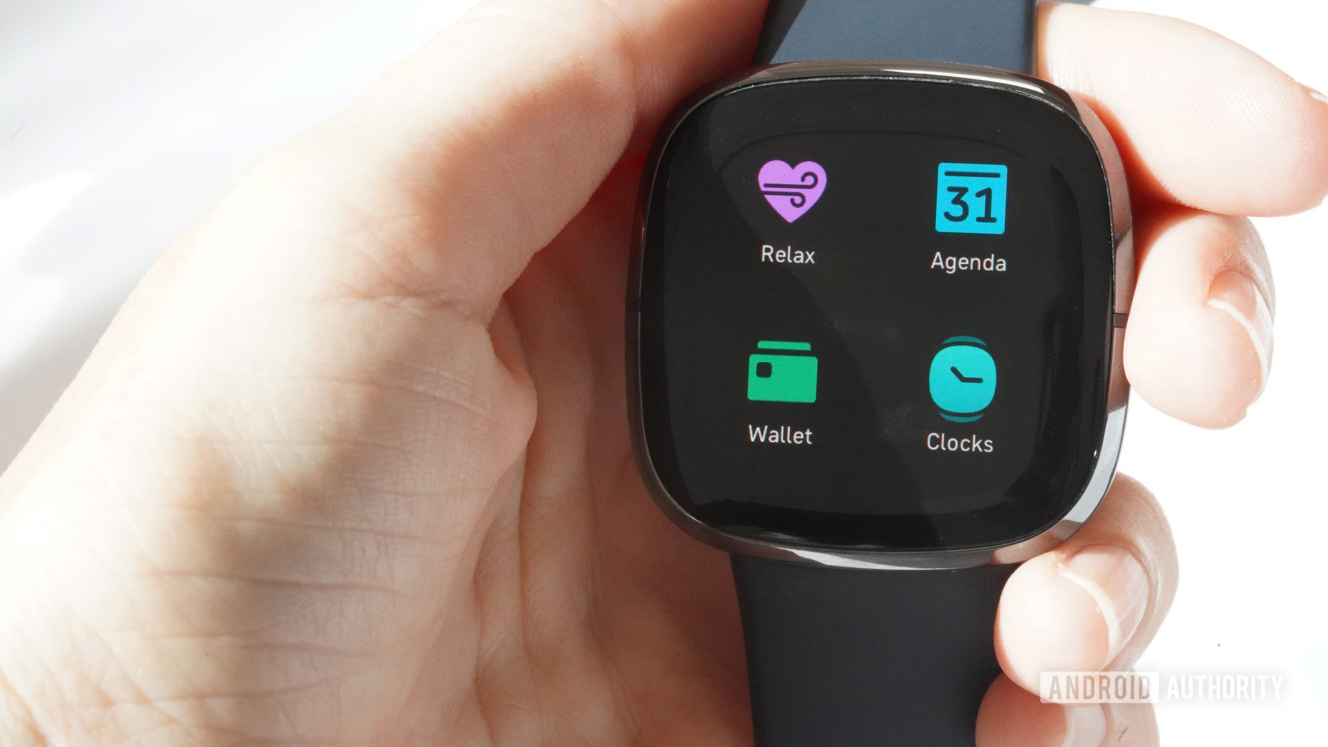 A Fitbit Sense in a user's hand displays the Wallet app.