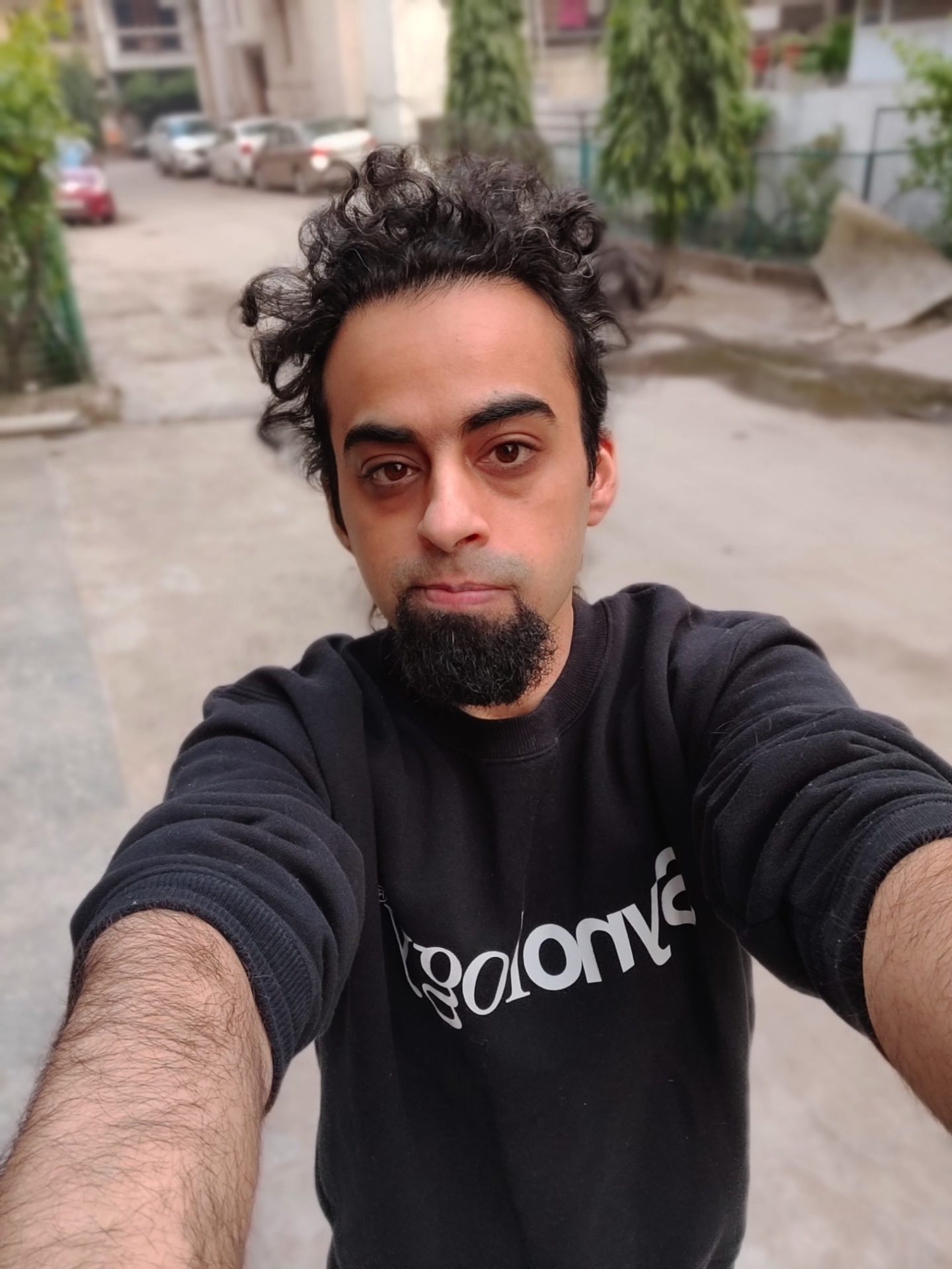 OnePlus 9RT selfie camera in portrait mode outside shot of a man with dark curly hair and a beard, wearing a black top