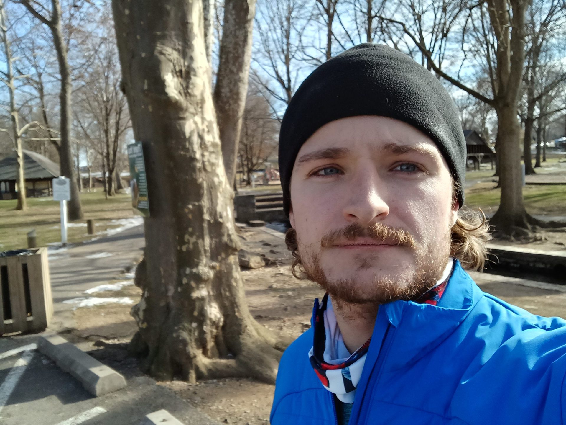 Galaxy A13 standard selfie taken outdoors of a man with facial hair wearing a black hat and a bright blue jacket
