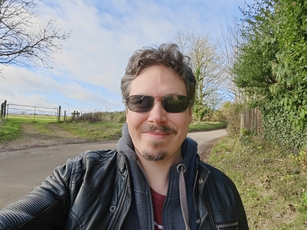 Huawei P50 Pro camera sample selfie outdoors of a man with brown hair and facial hair, wearing shades and a leather jacket with a hoodie underneath