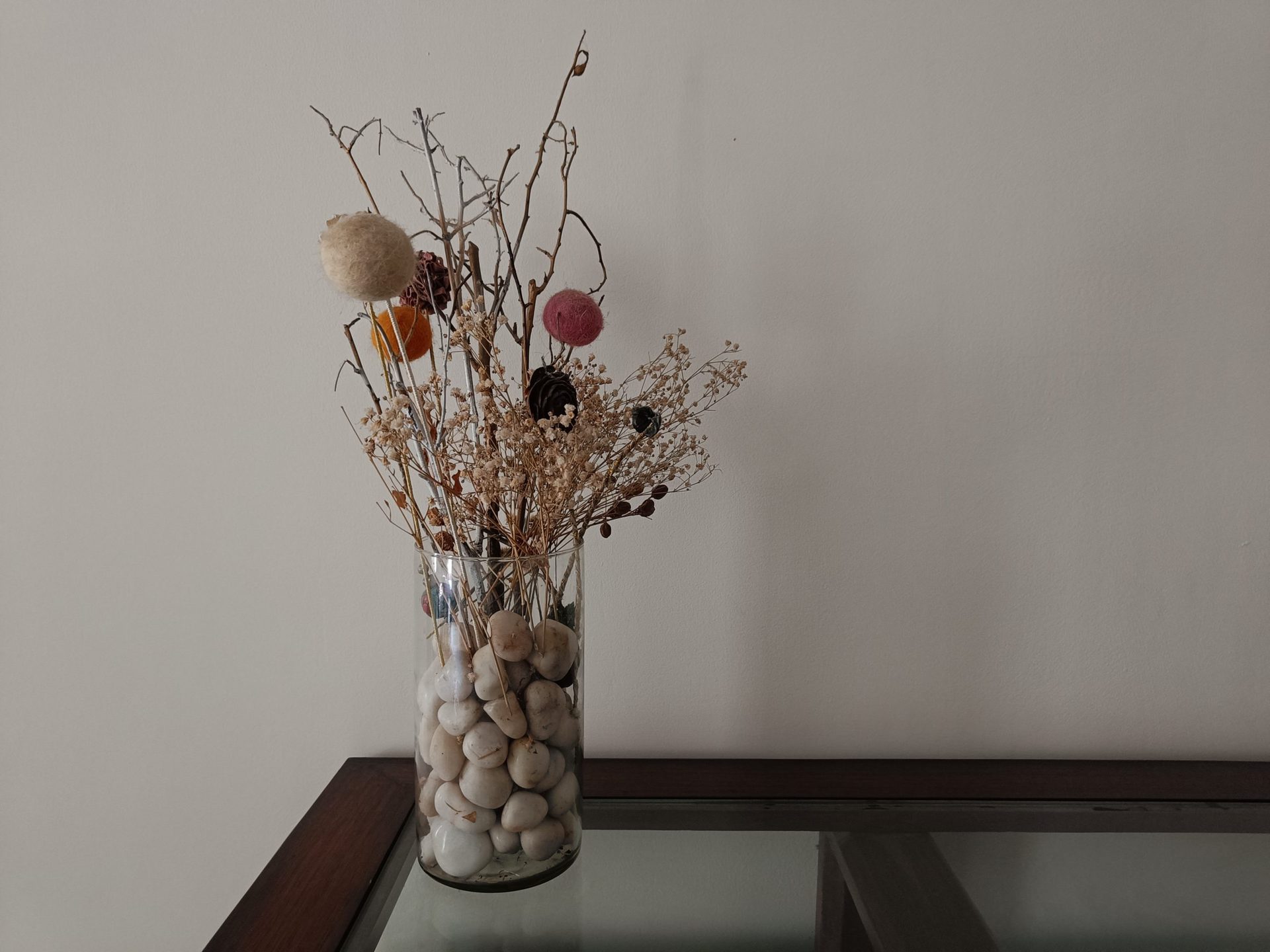 realme 9 Pro Plus dim light shot of a table with a glass vase on it containing pebbles and dried flowers.