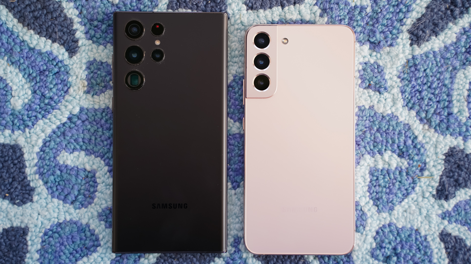 Samsung Galaxy S22 Ultra hitam vs Samsung Galaxy S22 Plus belakang merah muda di atas karpet