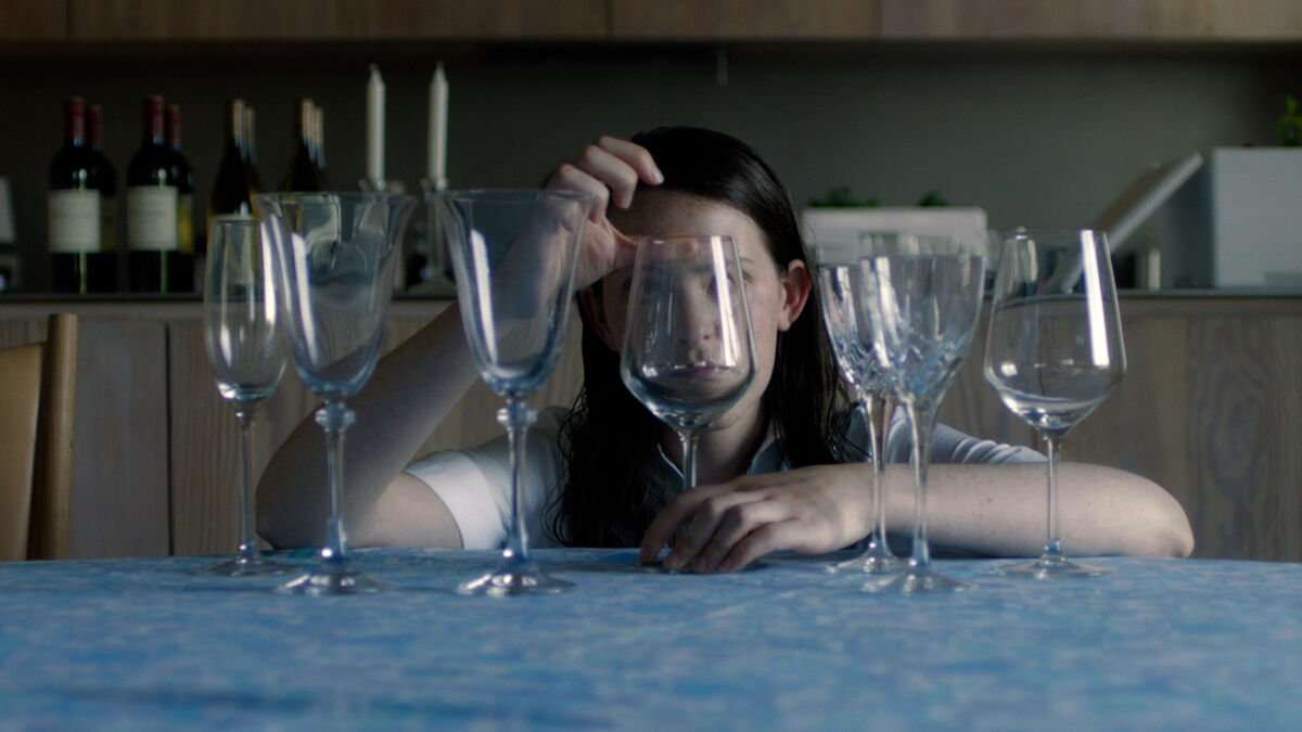 A woman sits behind several wine glasses in The Feast - best new streaming movies