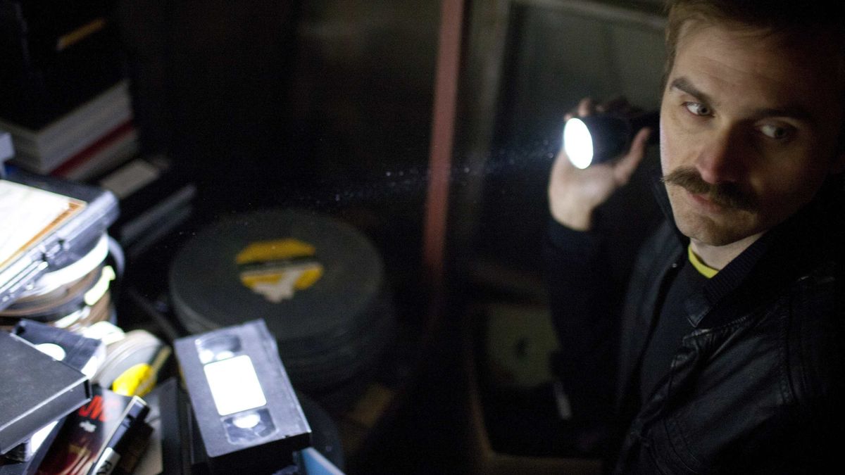 A cop with a flashlight looks at stacks of videotaped in VHS - movies like Archive 81