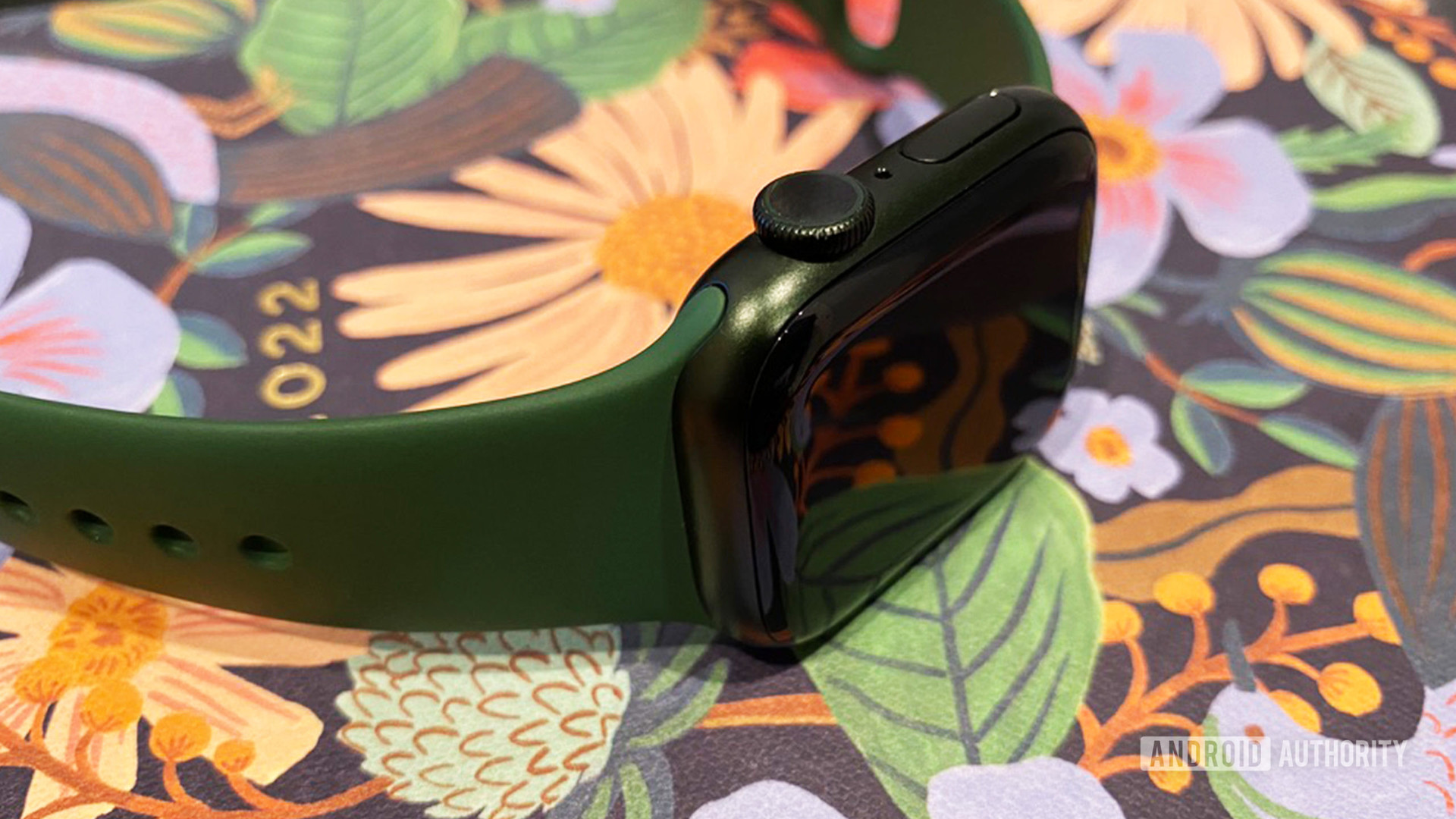 An Apple Watch Series 7 rests on it side on a floral planner, emphasizing the device's Digital Crown.