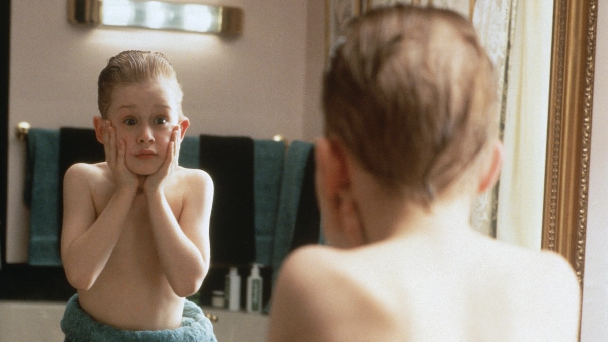 Macaulay Culkin applies aftershave while looking in the mirror in Home Alone - best family movies on disney plus