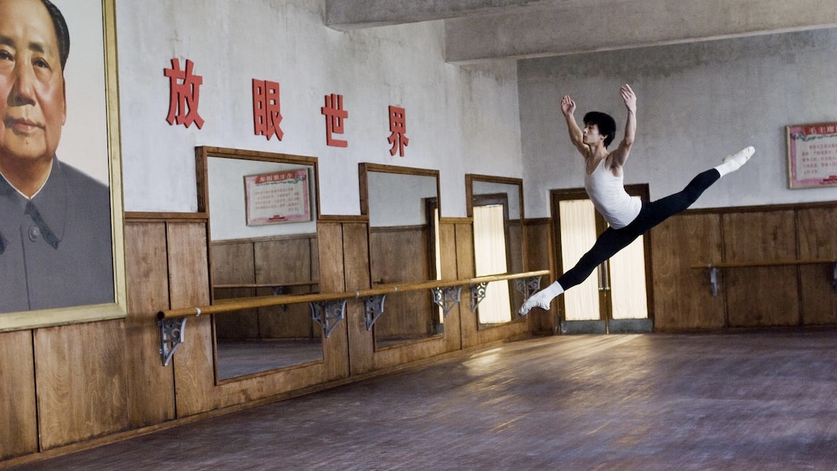 A lone dancer leeps in front of a portrait of Mao in Maos Last Dancer - best movies like CODA