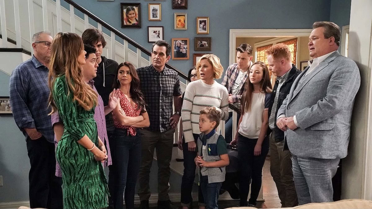 The cast of Modern Family stands together at the foot of the stairs in the Dunphy home