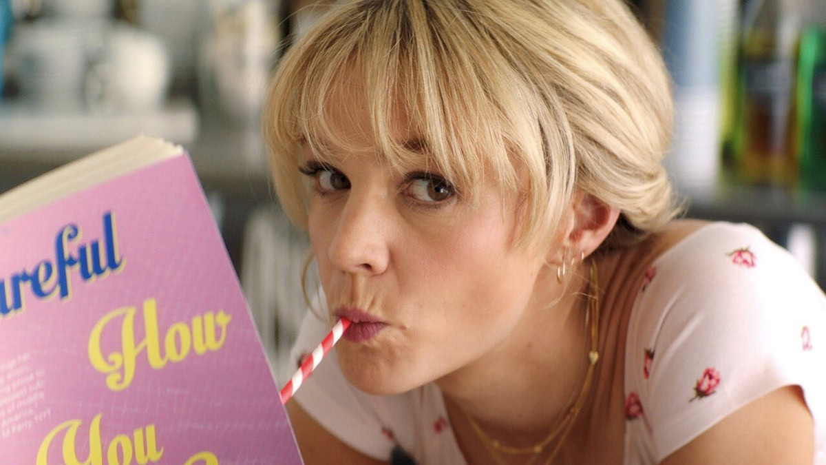 Carey Mulligan drinks from a straw while reading a book in Promising Young Woman