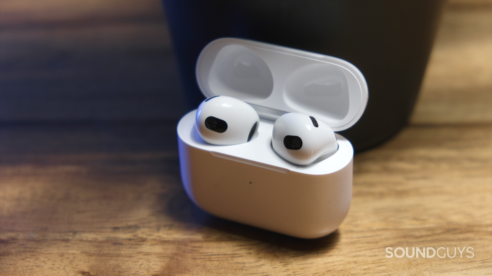 The open case of Apple AirPods (3rd generation) grips the earbuds and rests on a wooden surface.