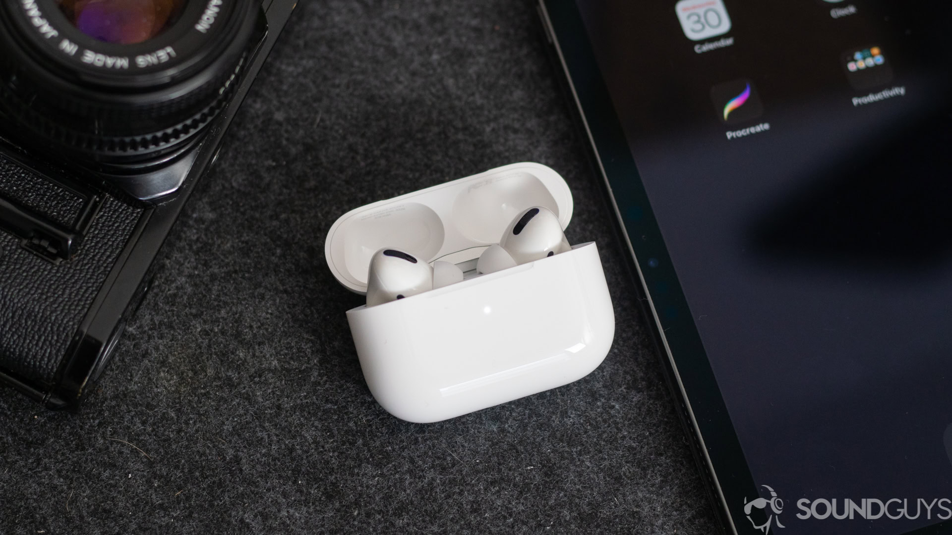 AirPods Pro earphones in the wireless charging case next to an iPhone and a digital camera.