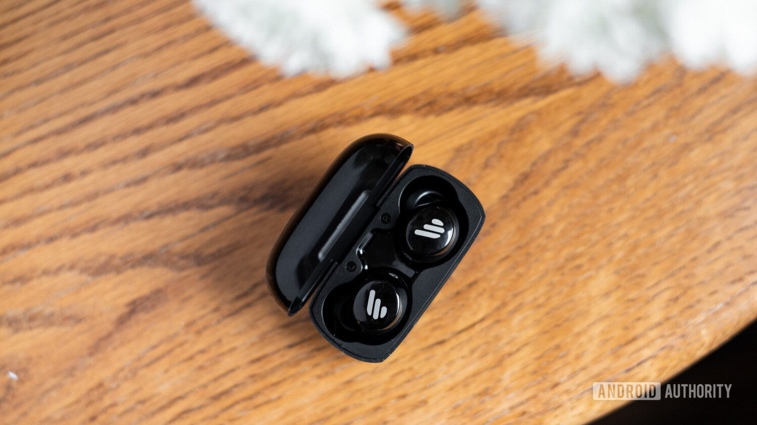 The Edifier TWS1 true wireless earbuds in the case on a wooden table.