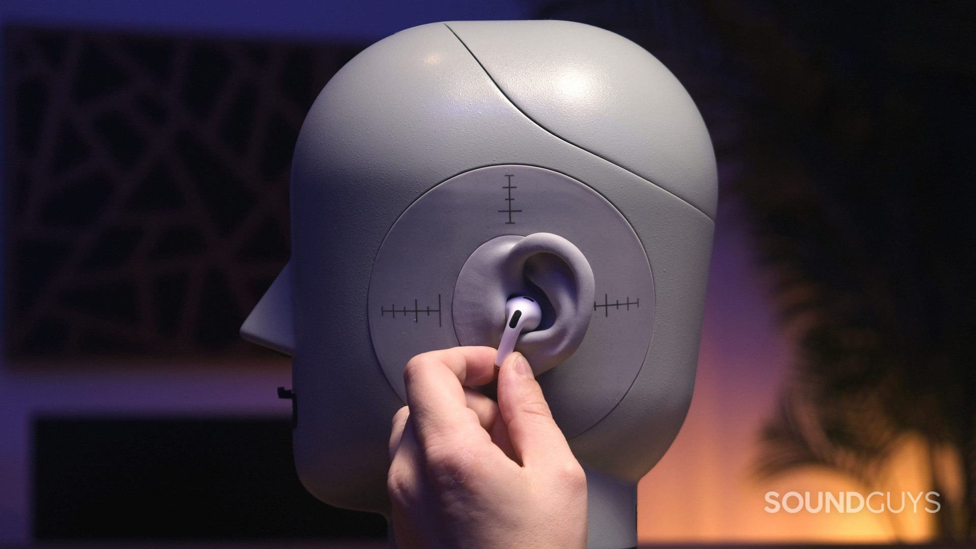 A hand holds one of the Apple AirPods (3rd generation) to the ear of a head simulator.