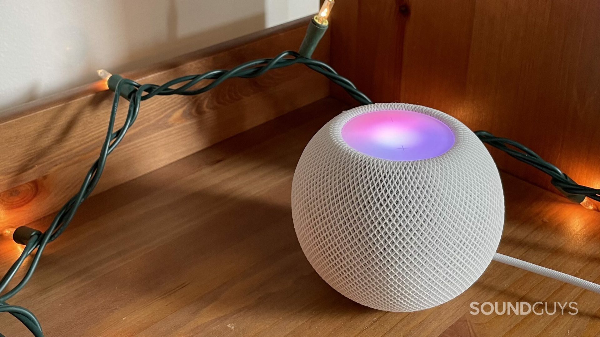 The HomePod mini on a wooden floor next to some lights.