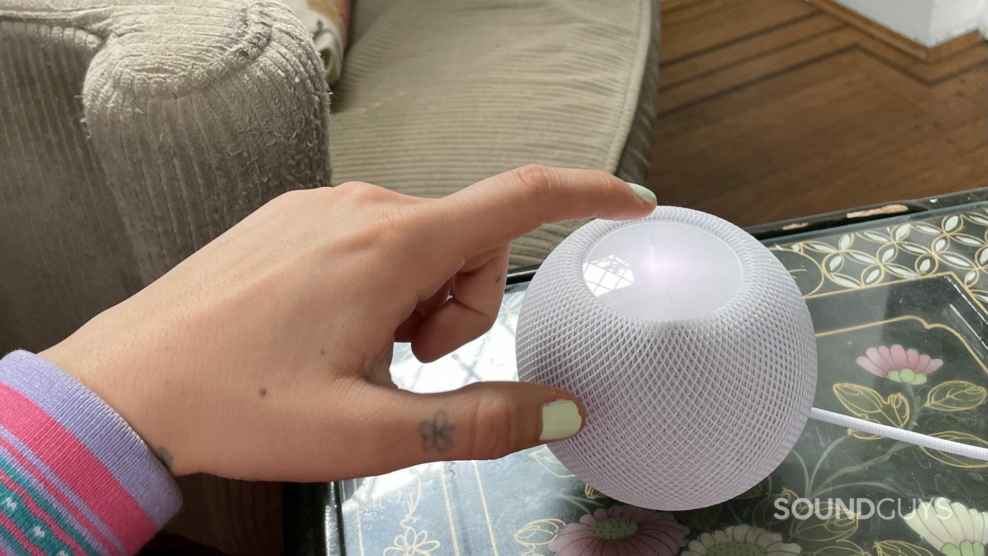 A hand touching the touch pad on a HomePod mini.