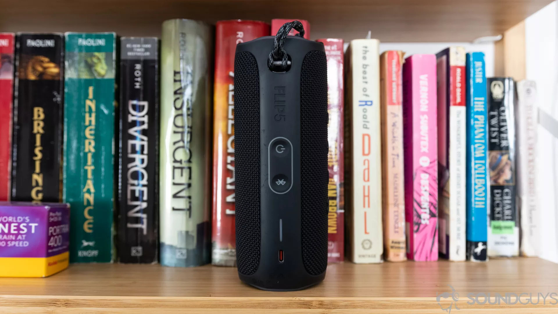 A JBL Flip 5 on bookshelf with the power button Bluetooth buttons visible.