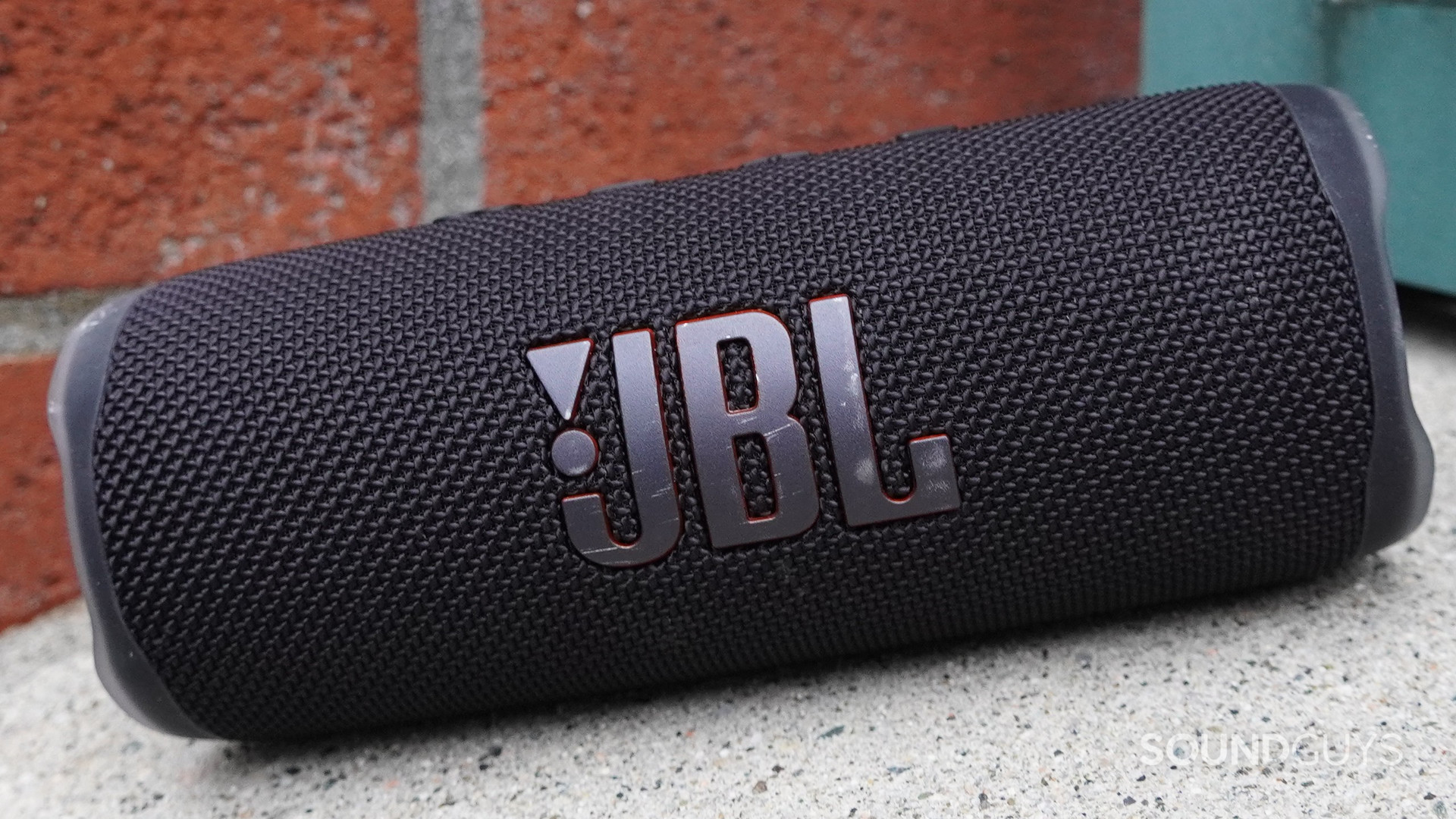 A JBL Flip 6 sitting on an inclied surface next to a brick wall.