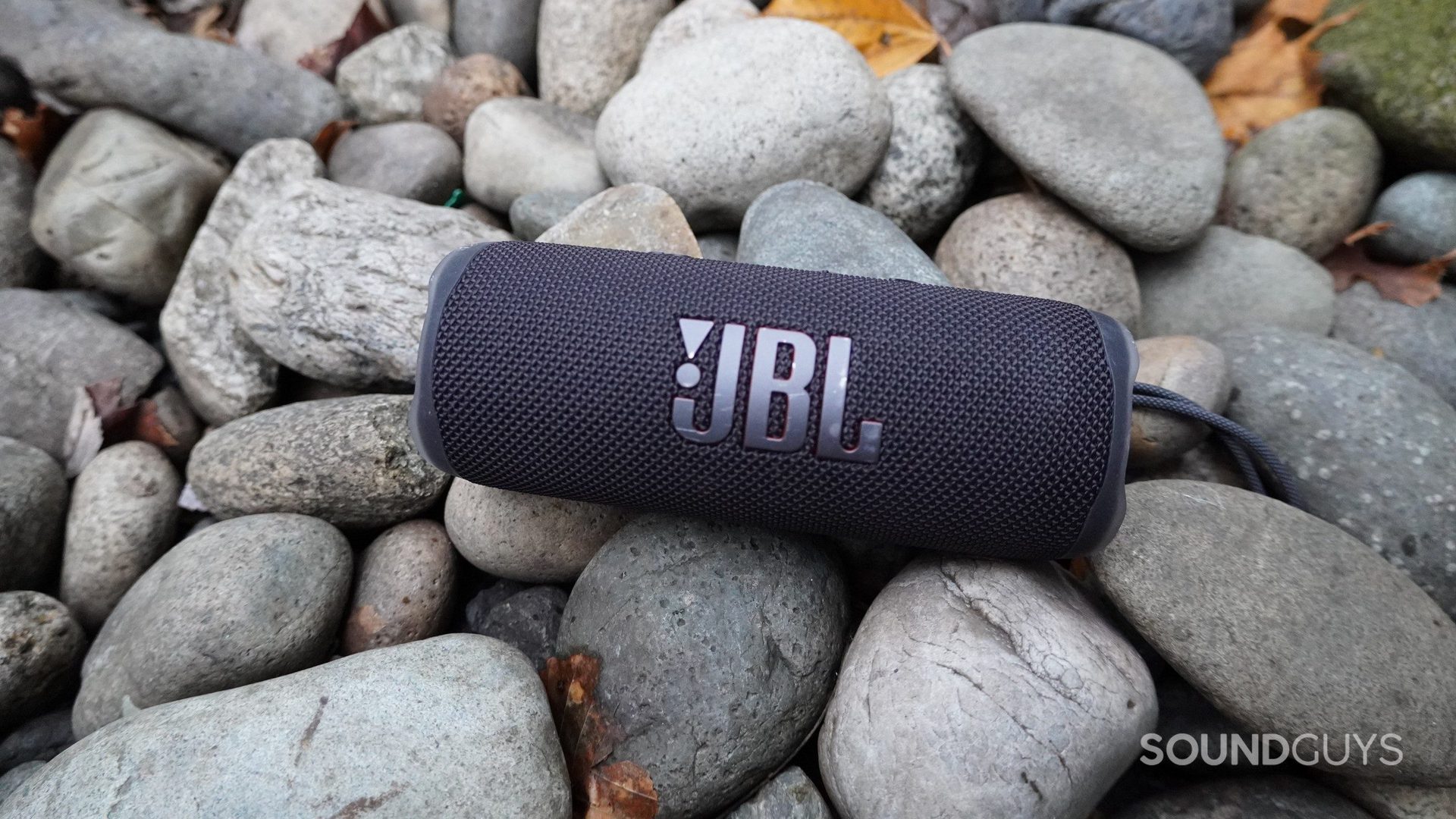 The JBL Flip 6 sittng on stones outdoors.