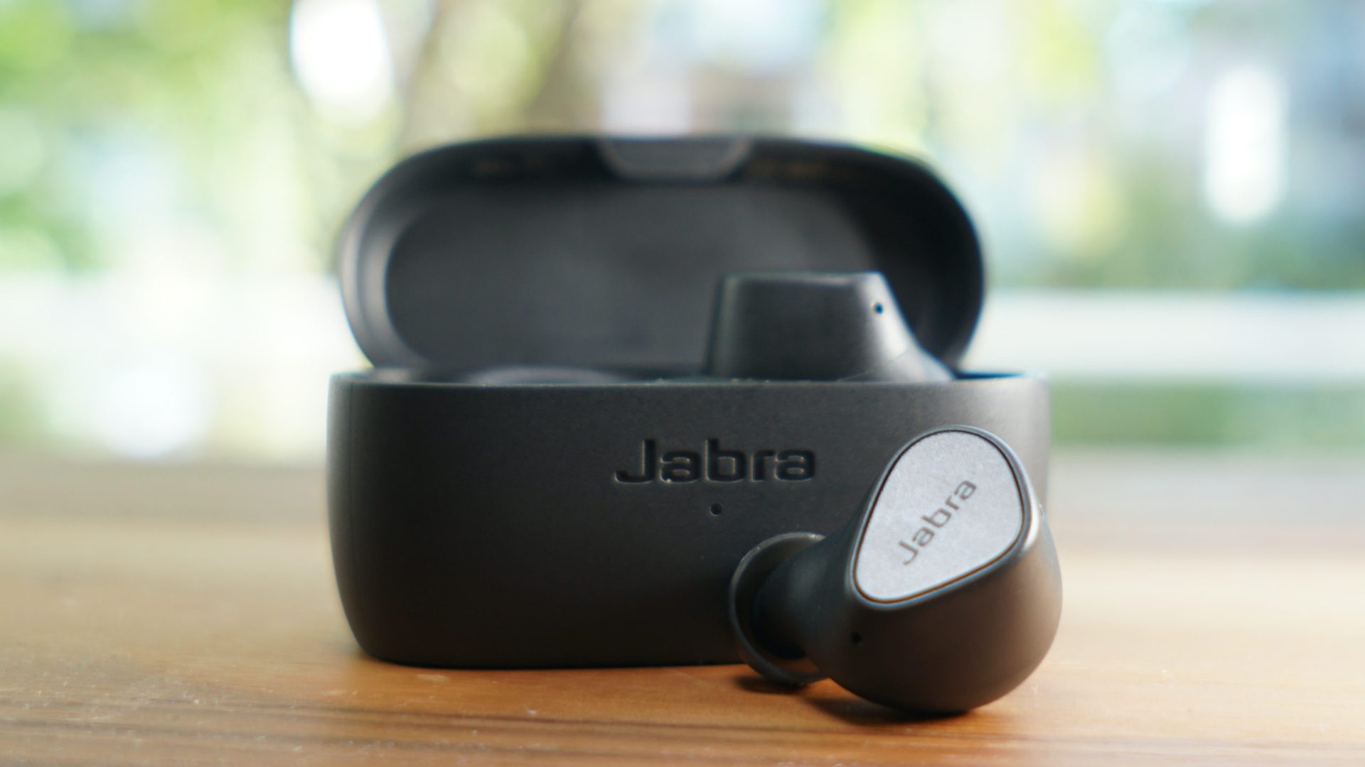 Jabra Elite 3, with one earbud placed on a table in front of the open case.