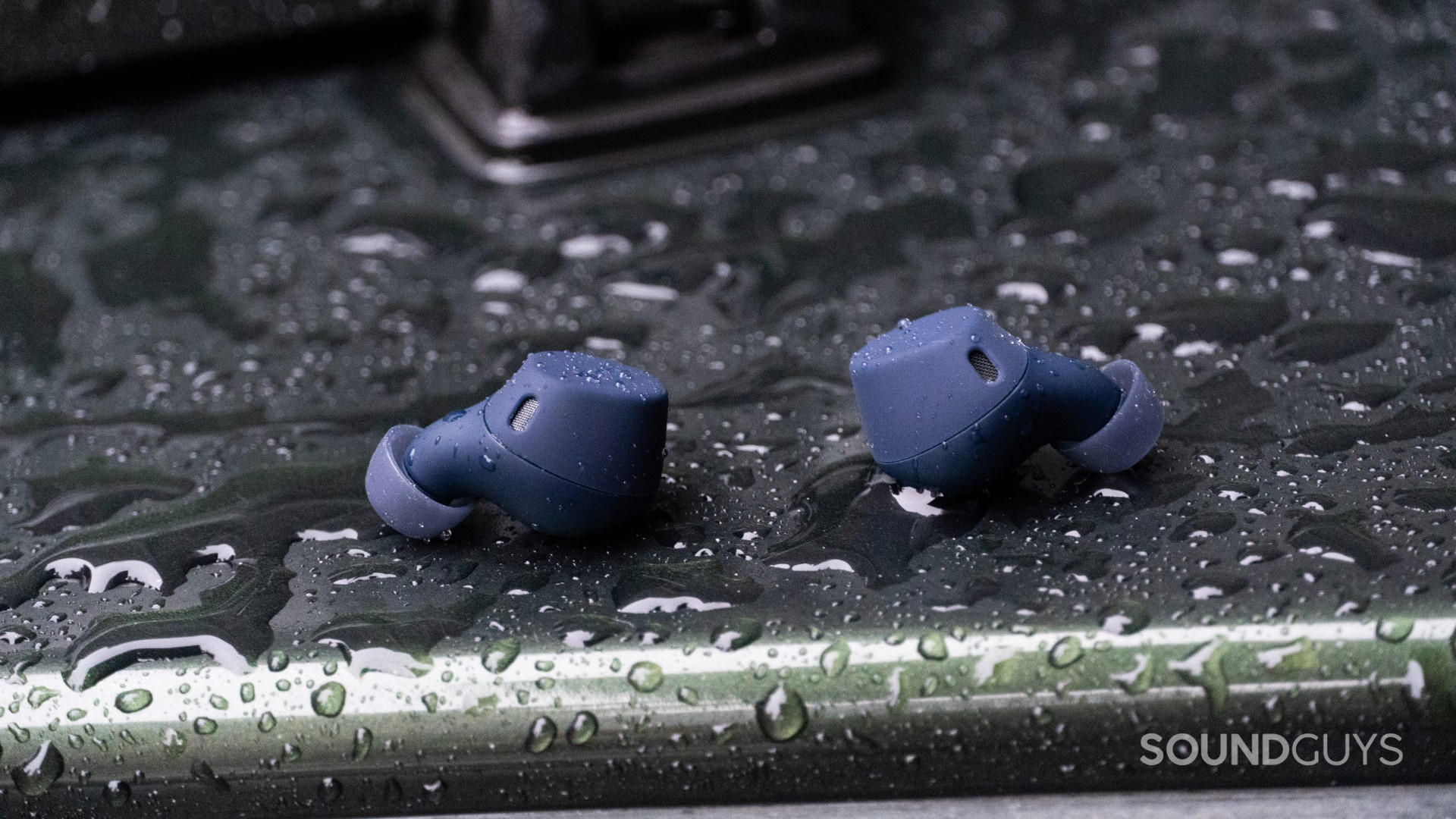 Jabra Elite 7 Active earbuds sitting on a rain-covered surface.
