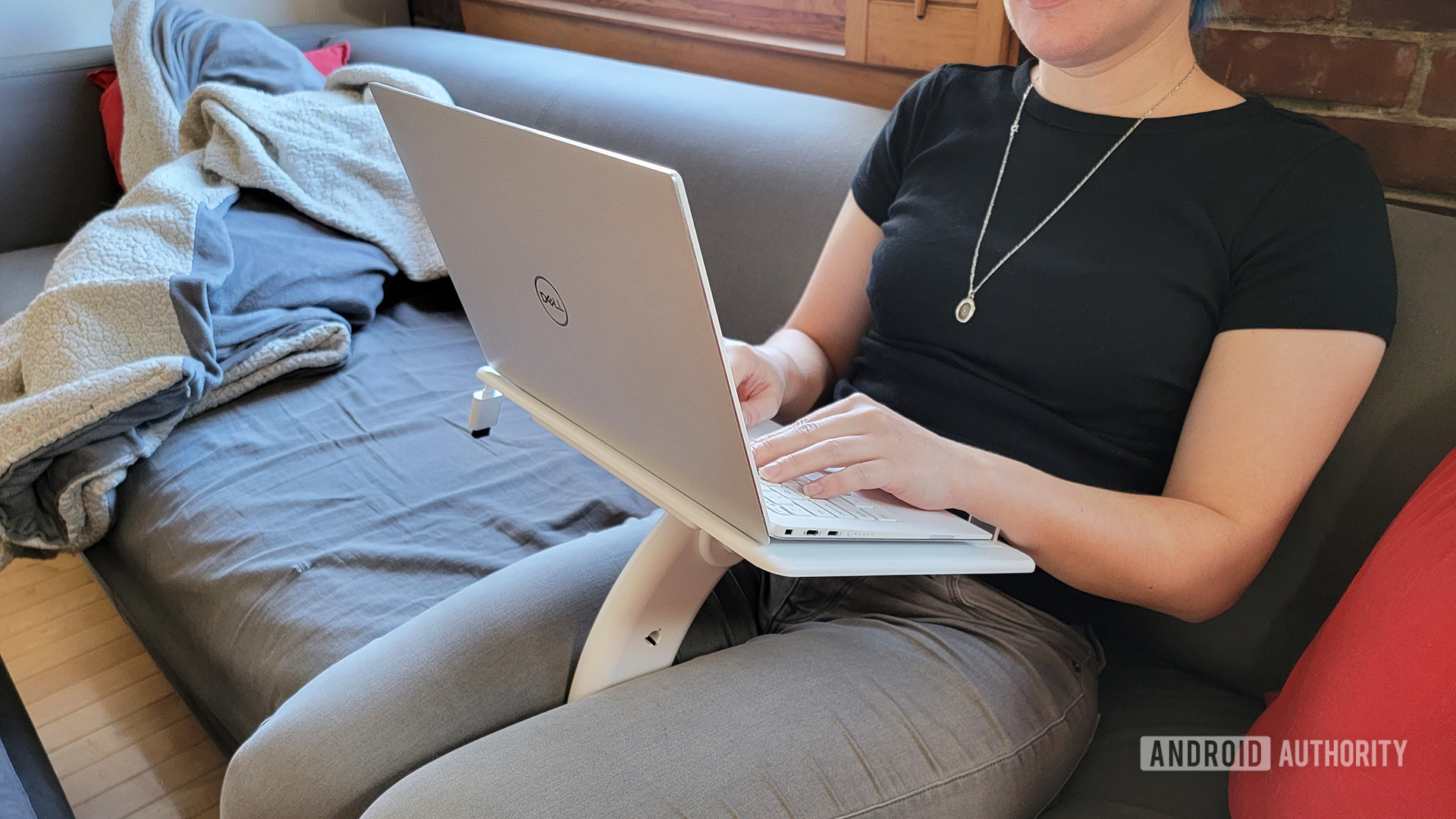 A woman sits with the Lamouple Lap Desk on her lap, with a Dell laptop on top.