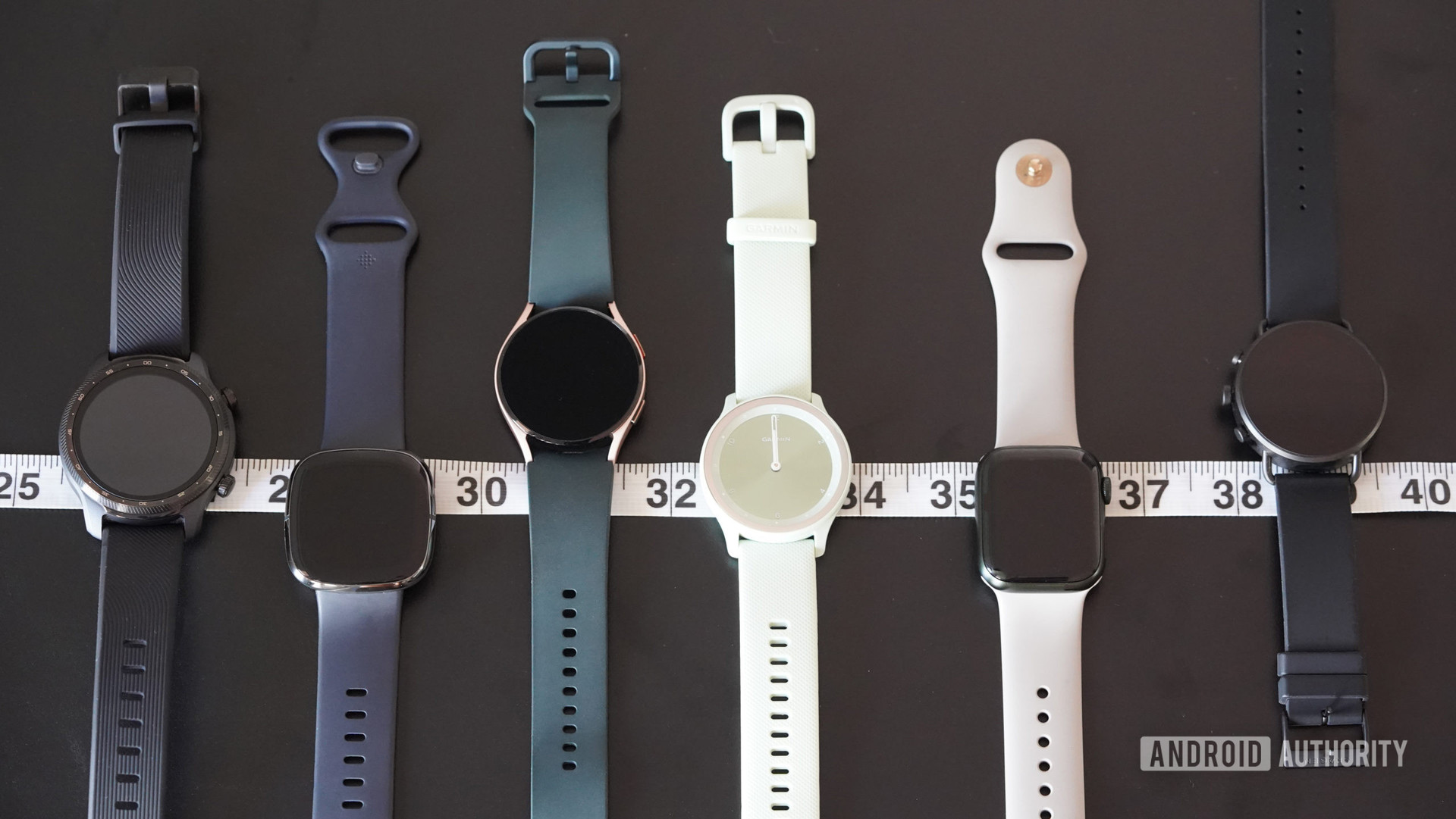 Apple Watch Series 7, Galaxy Watch 4, Garmin Vivomove Sport 등 다양한 스마트 시계가 측정 테이프를 따라 늘어서 있습니다.