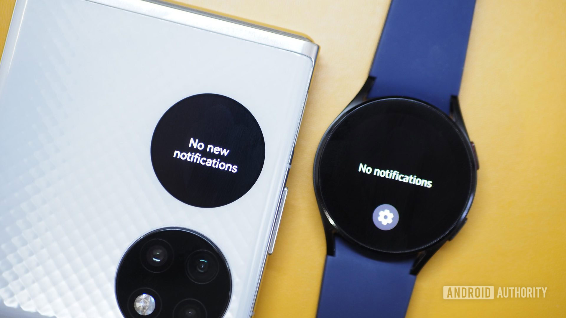 Huawei P50 Pocket white clamshell closed with no notifications on outer display next to Galaxy Watch 4 with no notifications