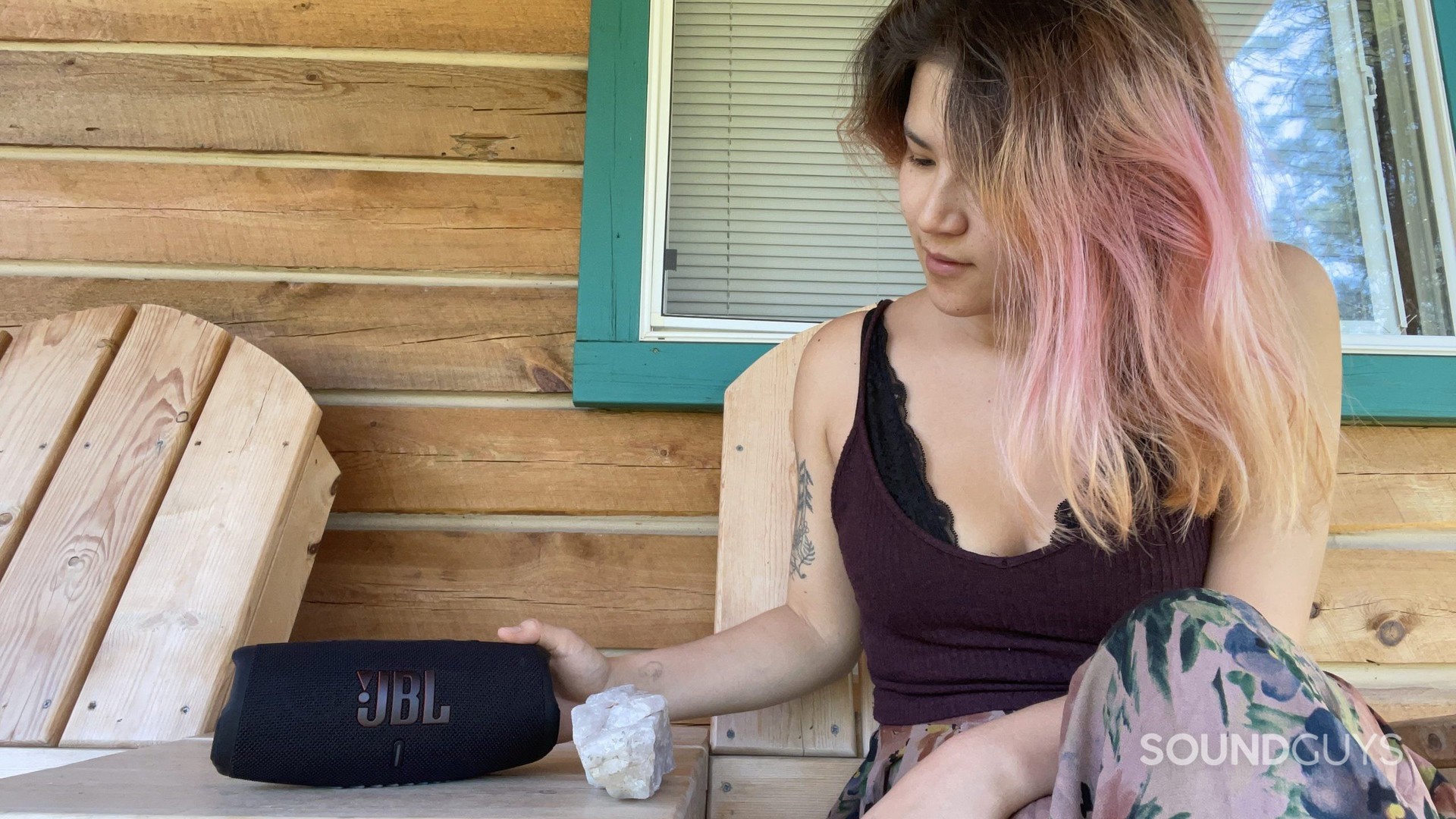 A woman touches the JBL Charge 5 as it rests on a table on a porch outdoors.