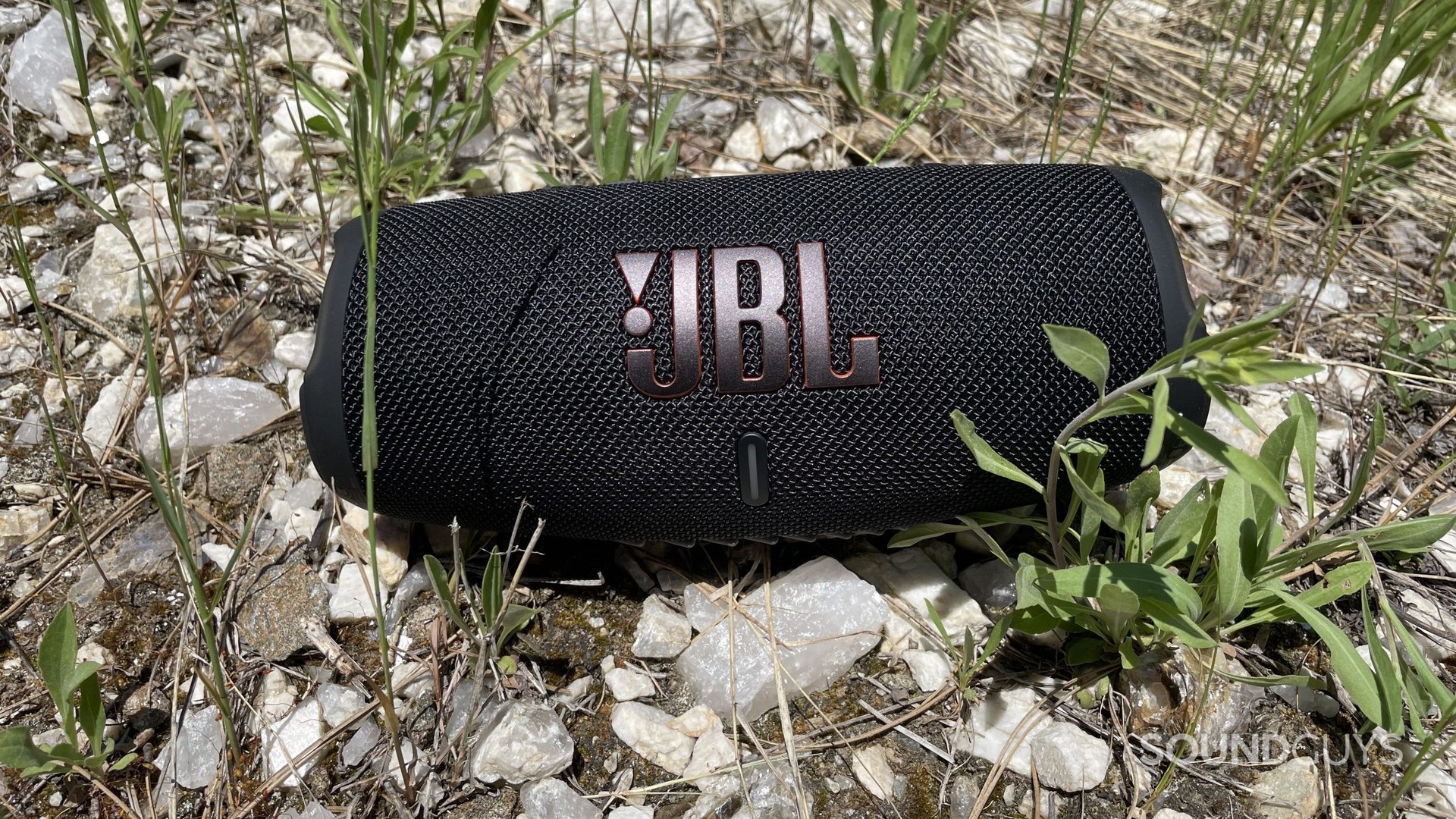 JBL Charge 5 reposant sur des rochers et de l'herbe.