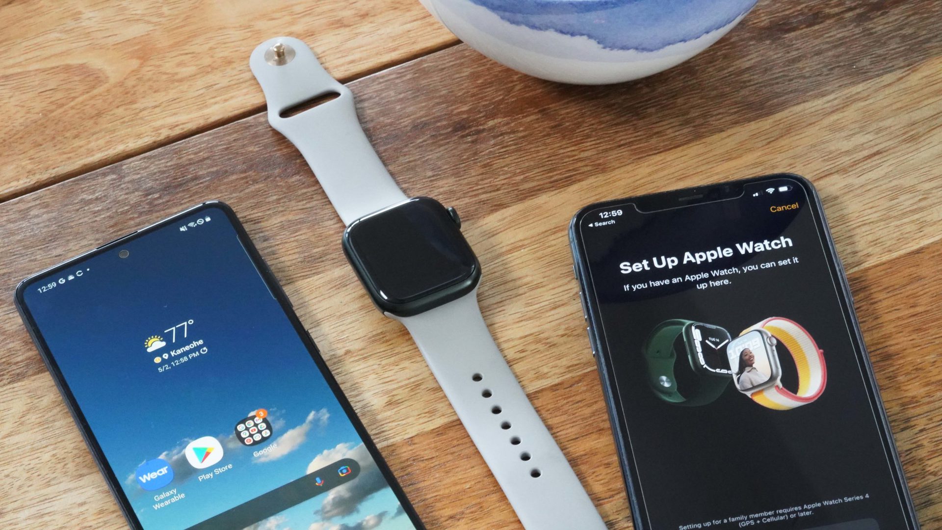 An Apple Watch Series 7 rests atop and Android phone and iPhone.