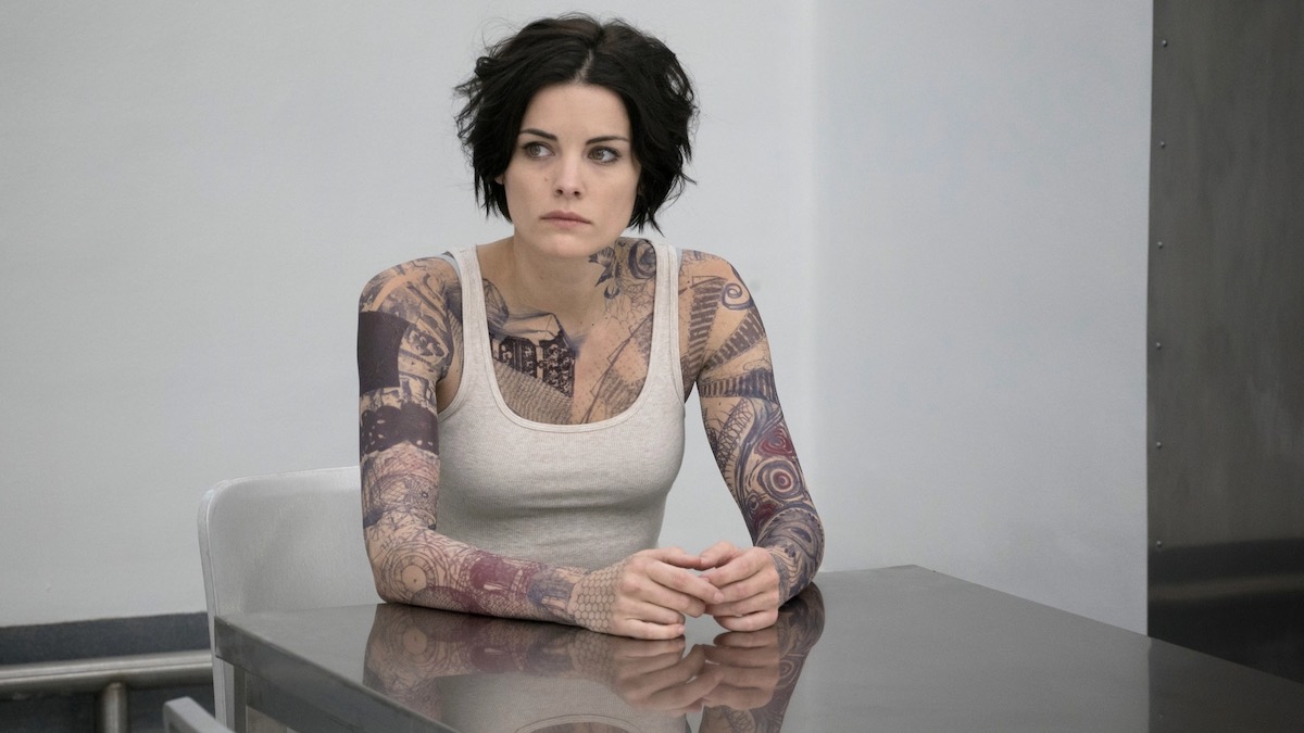 Jaimie Alexander sits at a table in a police station in Blindspot - shows like Moon Knight
