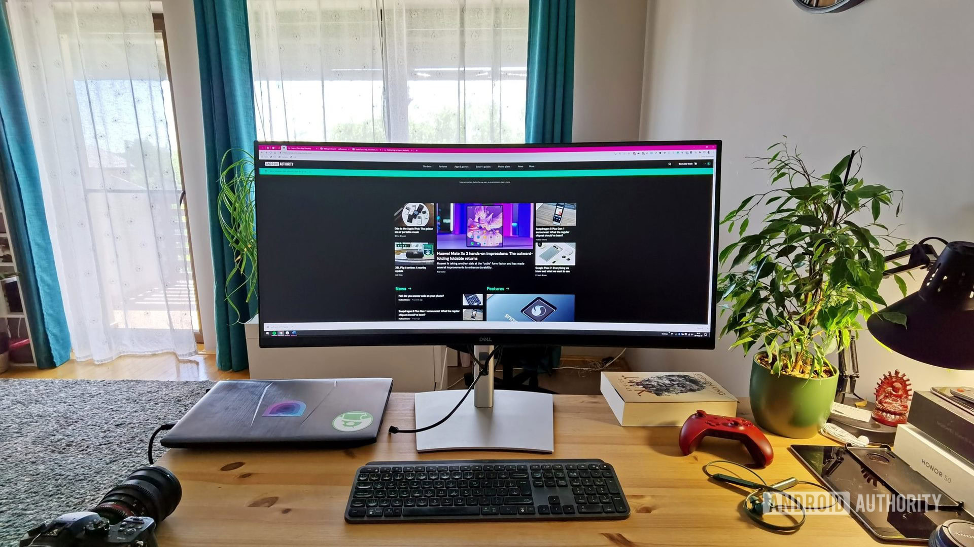 Dell P3421W ultrawide monitor on a desk with laptop, keyboard, lamp, and other accessories.