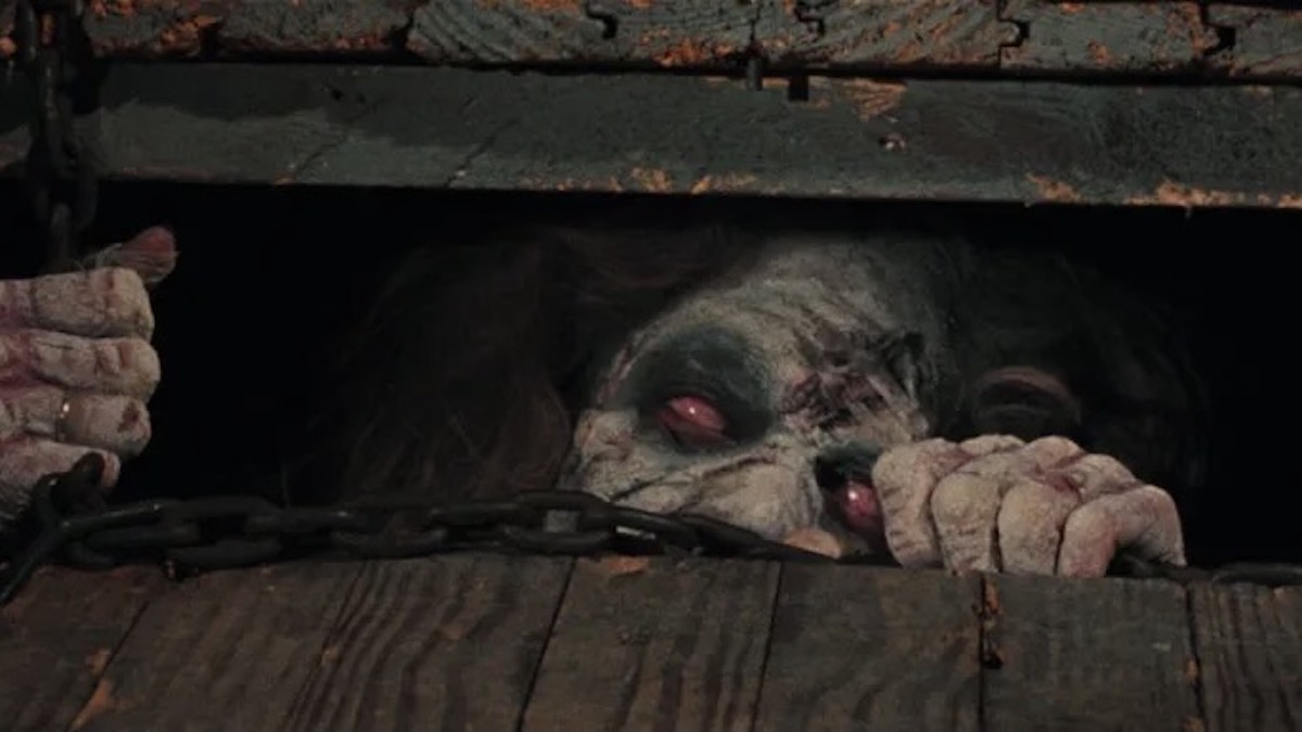 An undead woman looks out from a trap door in The Evil Dead