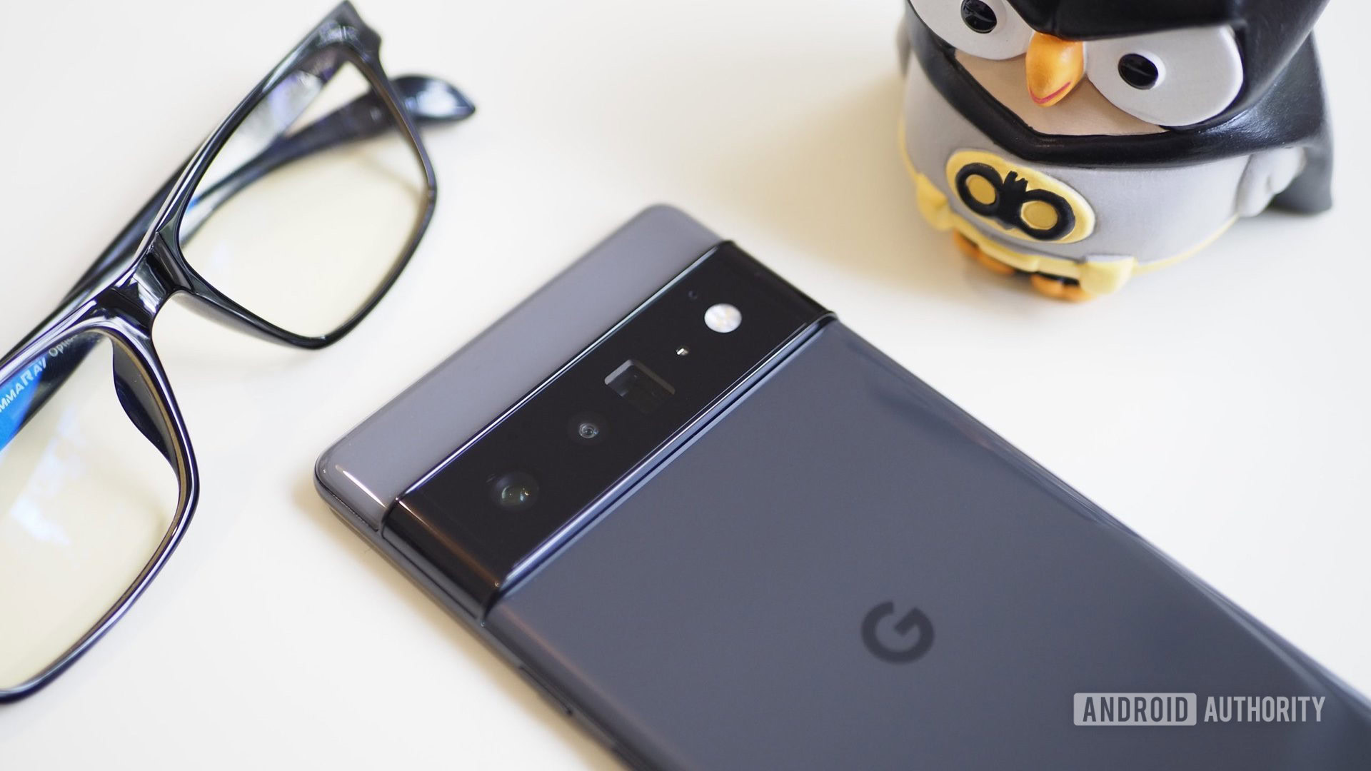 The face of the Google Pixel 6 Pro is next to the glasses and a statue of Batman.