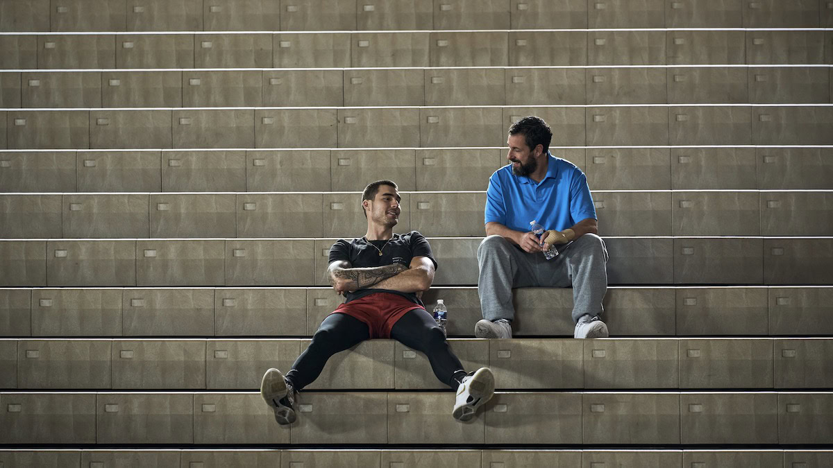 Juancho Hernangomez as Bo Cruz and Adam Sandler as Stanley Sugerman sitting in the bleachers in Hustle - best new streaming movies