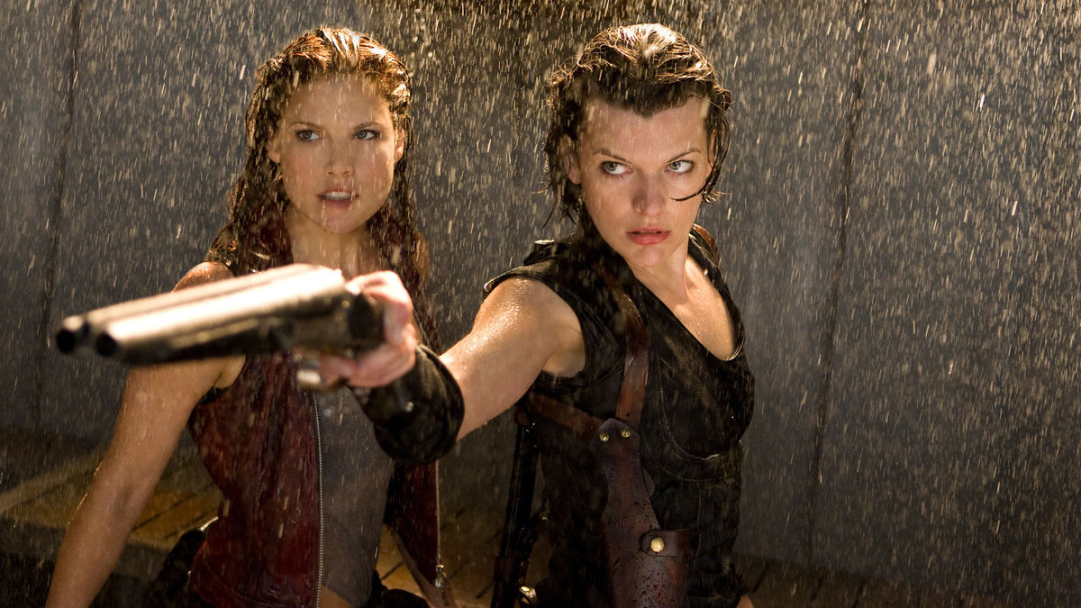 Milla Jovovich mengarahkan senapan dan berdiri dengan Ali Larter di bawah air yang jatuh di Resident Evil: Afterlife
