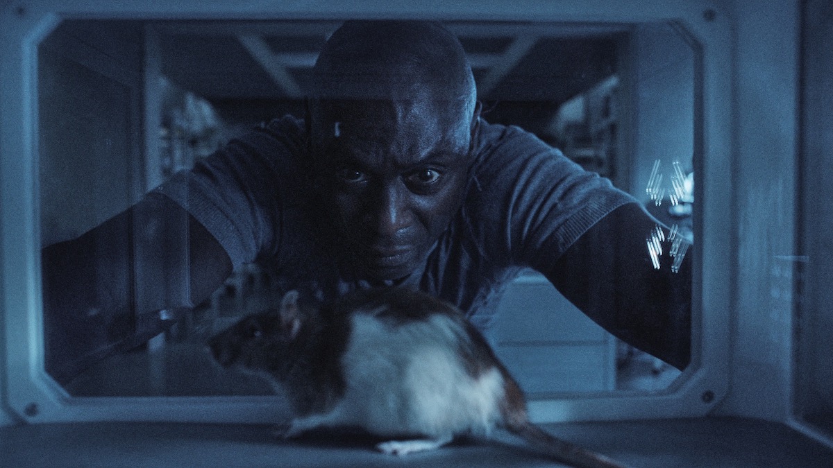 Lance Reddick looks at a rat in a cage in Resident Evil