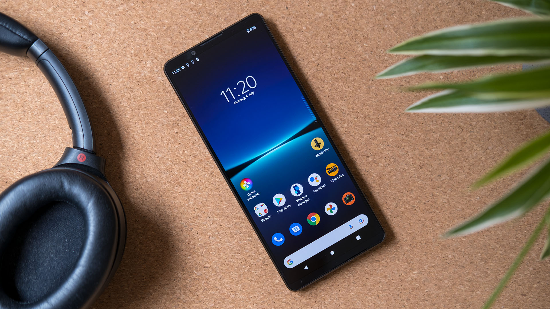 A Sony Xperia 1 IV showing its homescreen resting next to a pair of headphones and a plant.