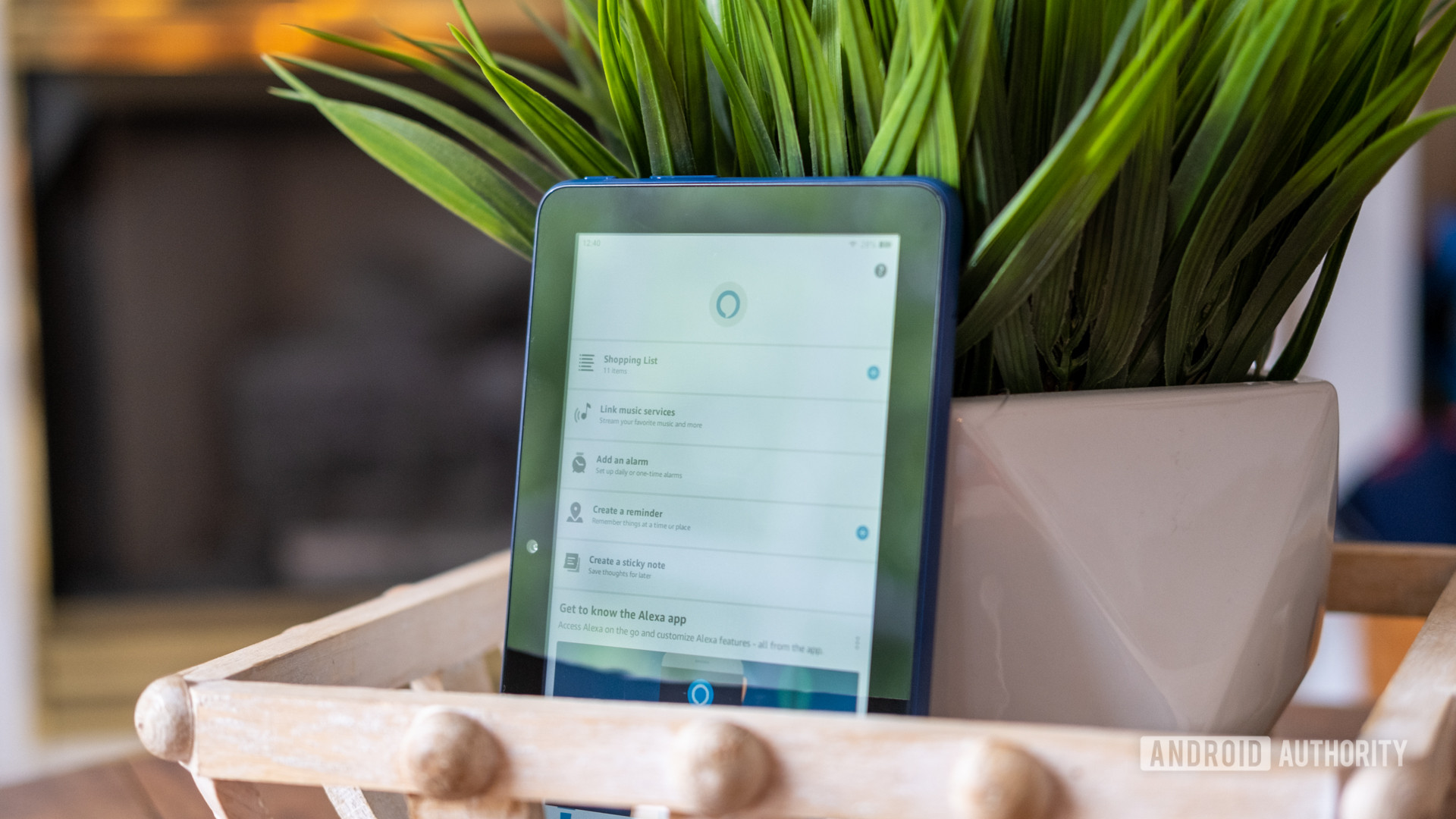 The amazon fire 7 2022 tablet propped up vertically against a plant pot showing the screen displaying the Alexa app 