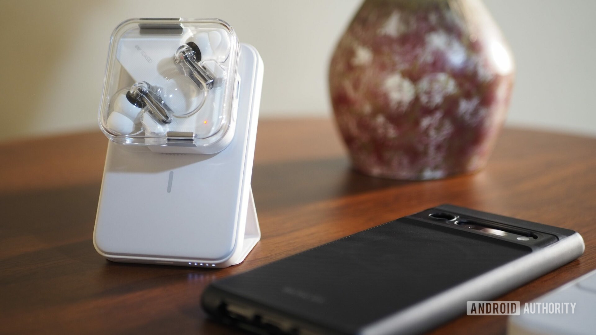Baterai Magnetik Anker 622 Putih disangga dengan pop-up stand di atas meja yang mengisi daya kuncup Nothing Ear (1), dengan Pixel 6 Pro di sebelahnya