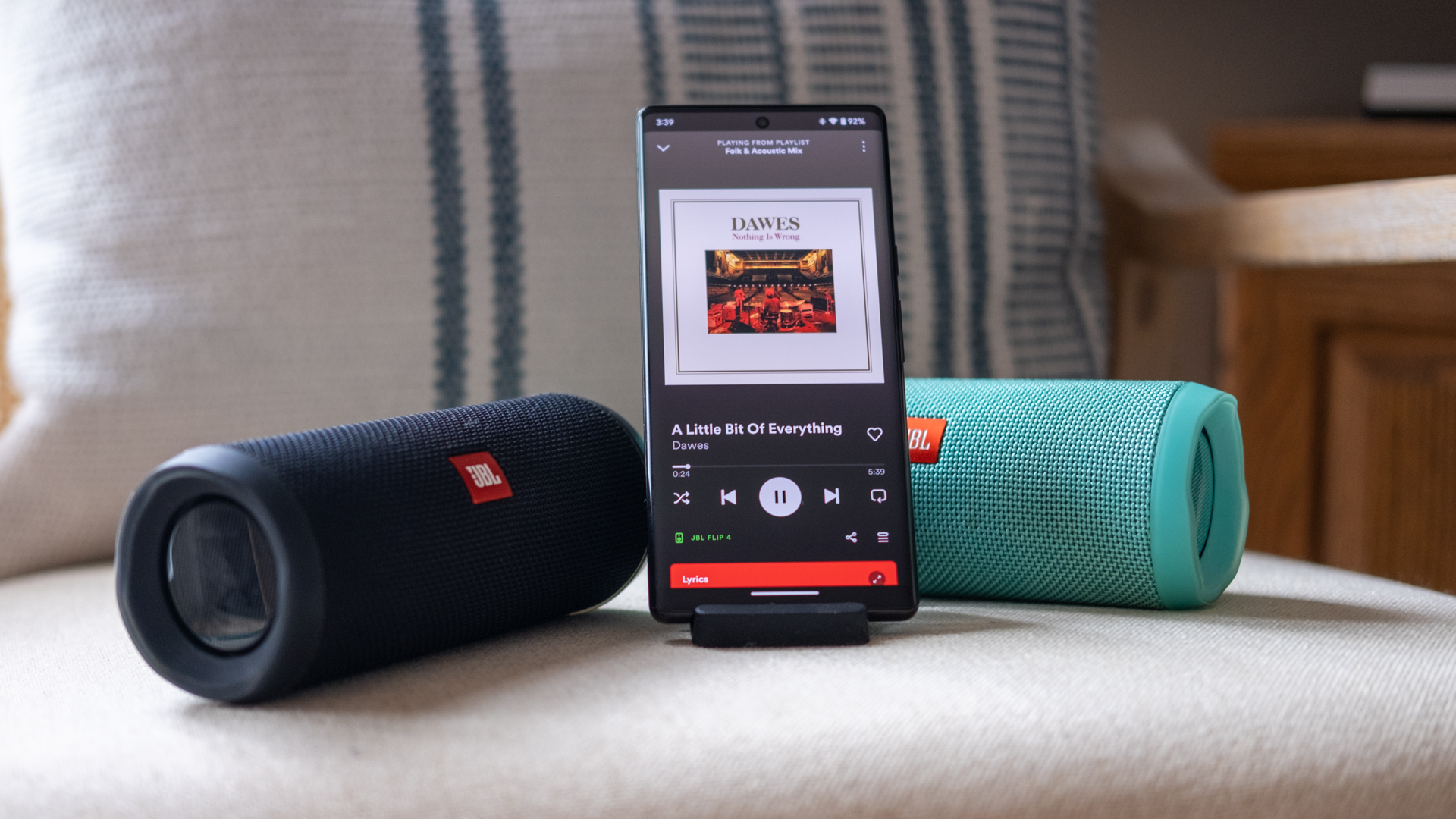 Dua speaker JBL Connect, satu biru, satu hitam, di kedua sisi ponsel memutar musik dari aplikasi Spotify.