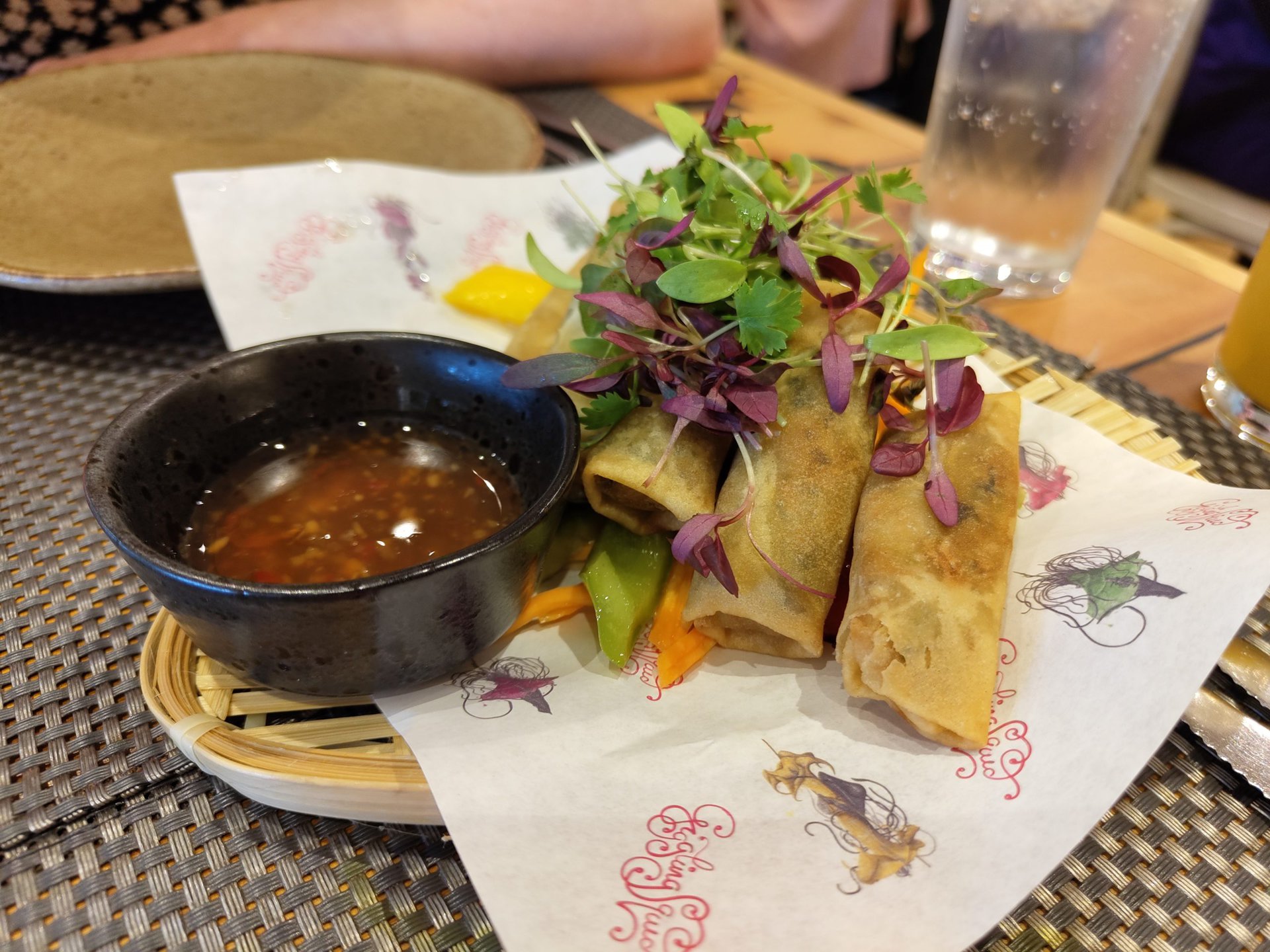 A plate of some crispy rolls and dipping sauce sitting on a table in a restaurant.