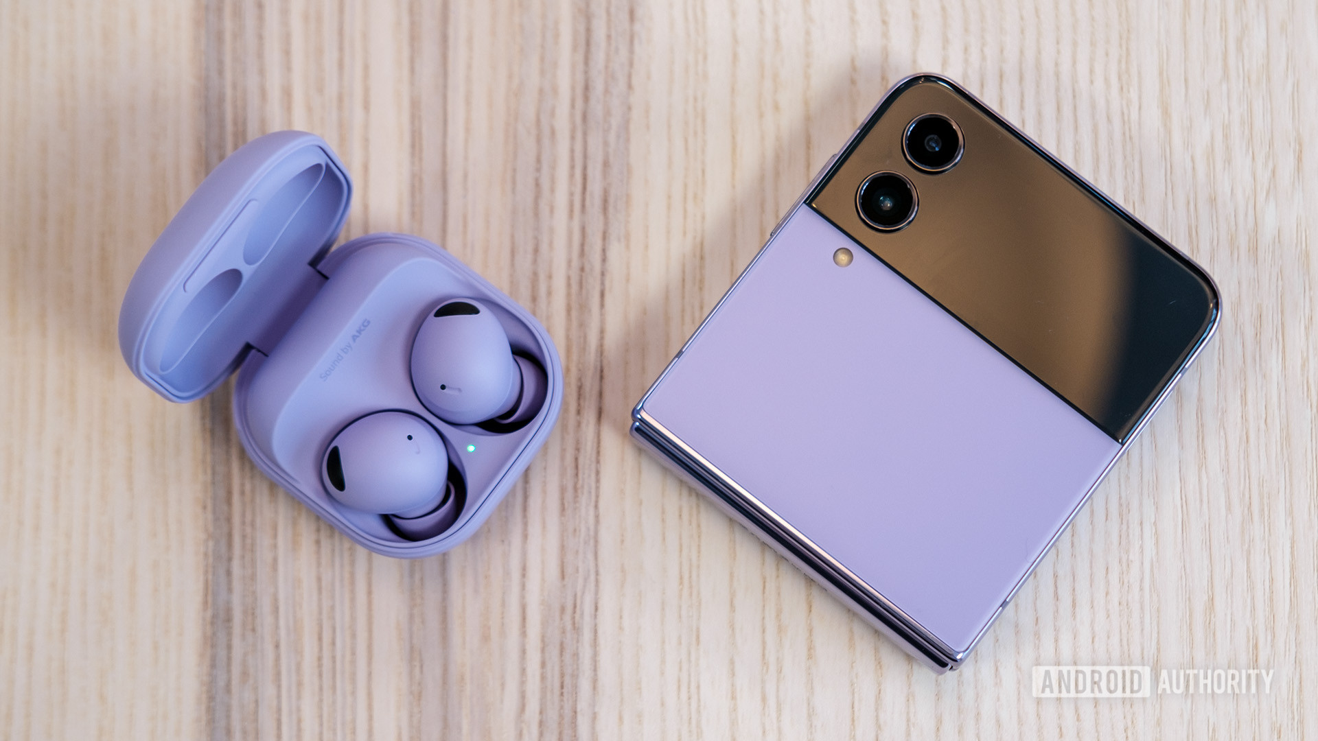 The Samsung Galaxy Buds 2 Pro in Bora Purple in their case next to a Galaxy Z Flip 4 in the same color on a wooden table.