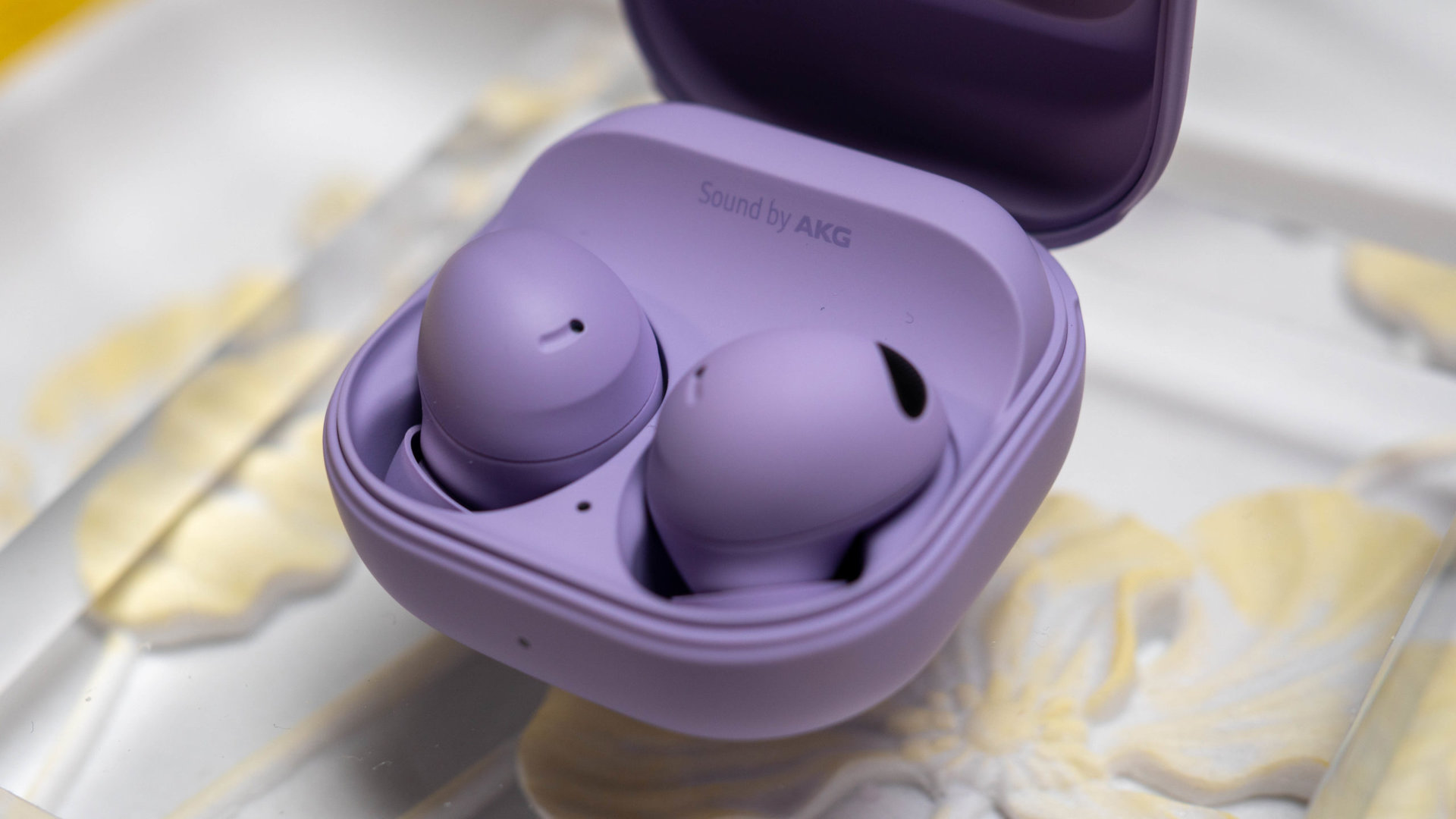 The Samsung Galaxy Buds 2 Pro in Bora Purple in their case on a glass display case.
