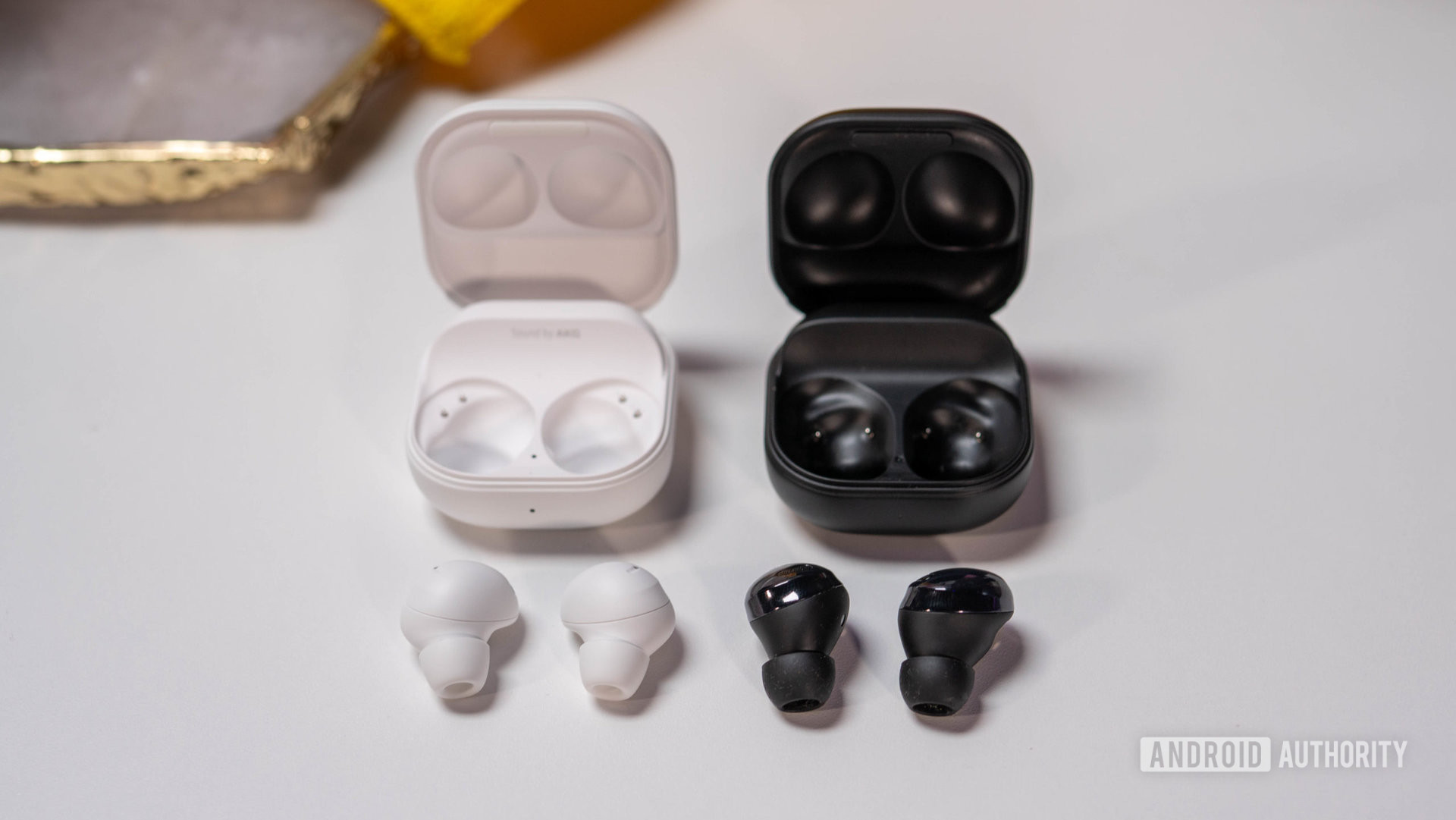 The Samsung Galaxy Buds 2 Pro and Samsung Galaxy Buds Pro laying on table with their charging cases above them.