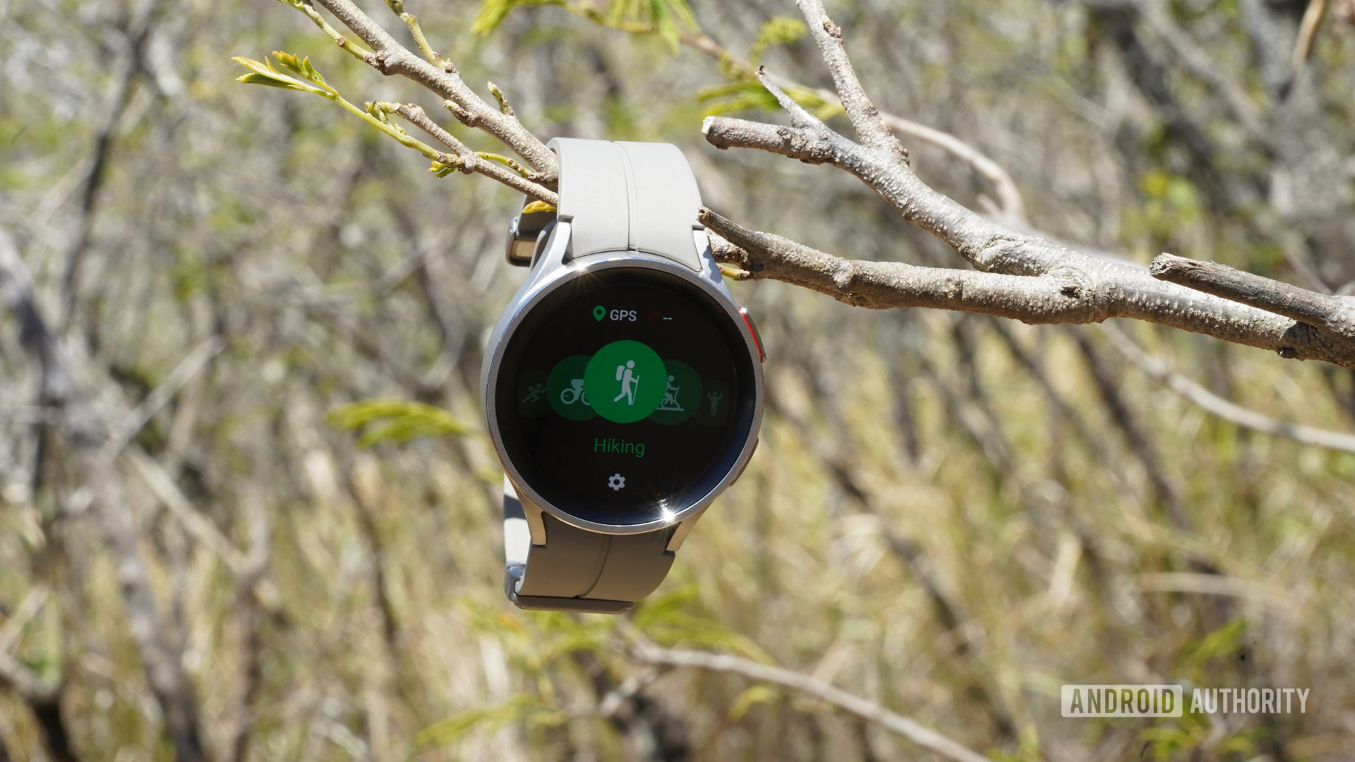 A Samsung Galaxy Watch 5 Pro hangs from a branch and displays the device's sports mode menu.