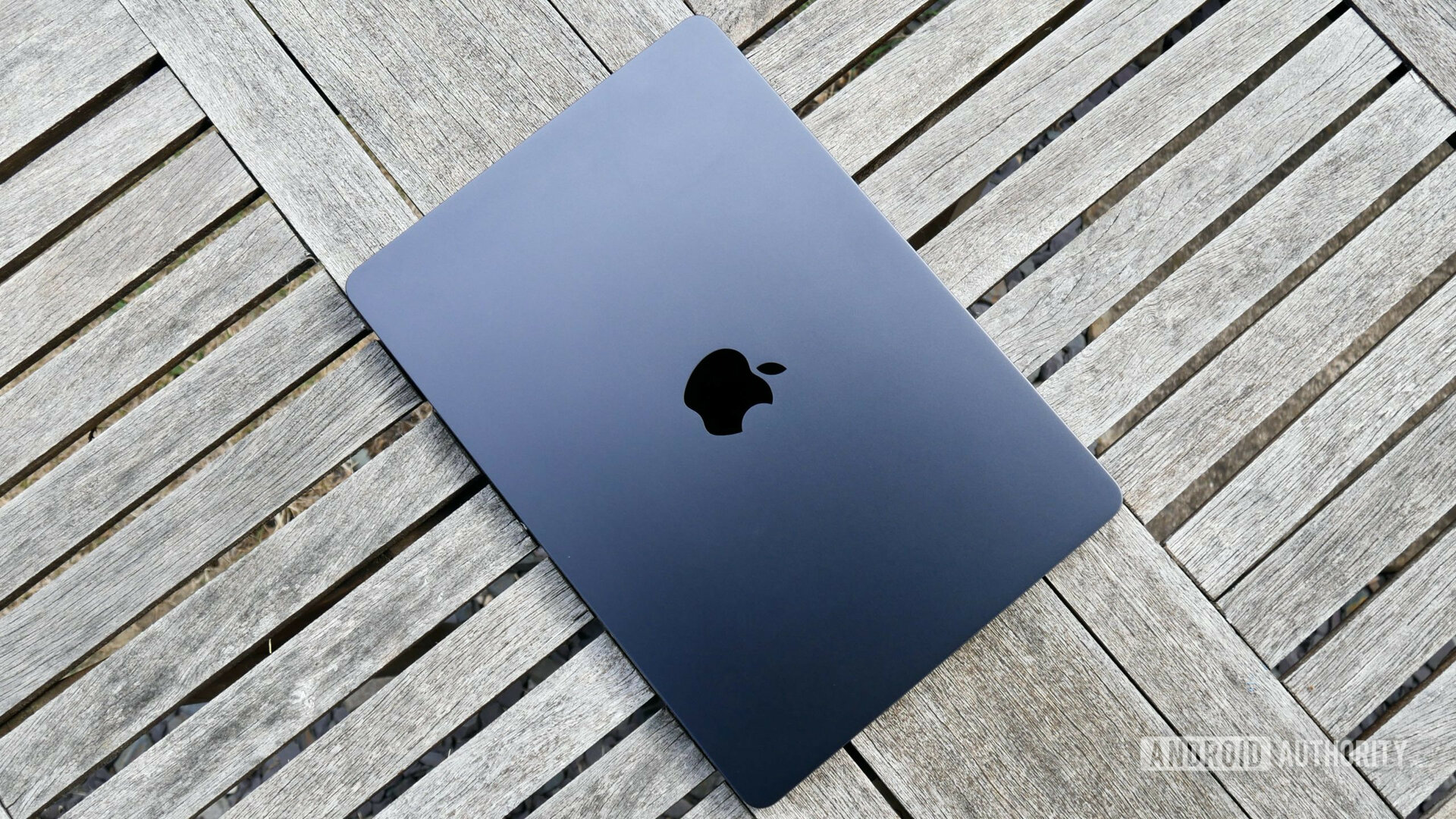 A dark-gray Apple MacBook Air M2 closed lying on top of a light-gray wooden deck.
