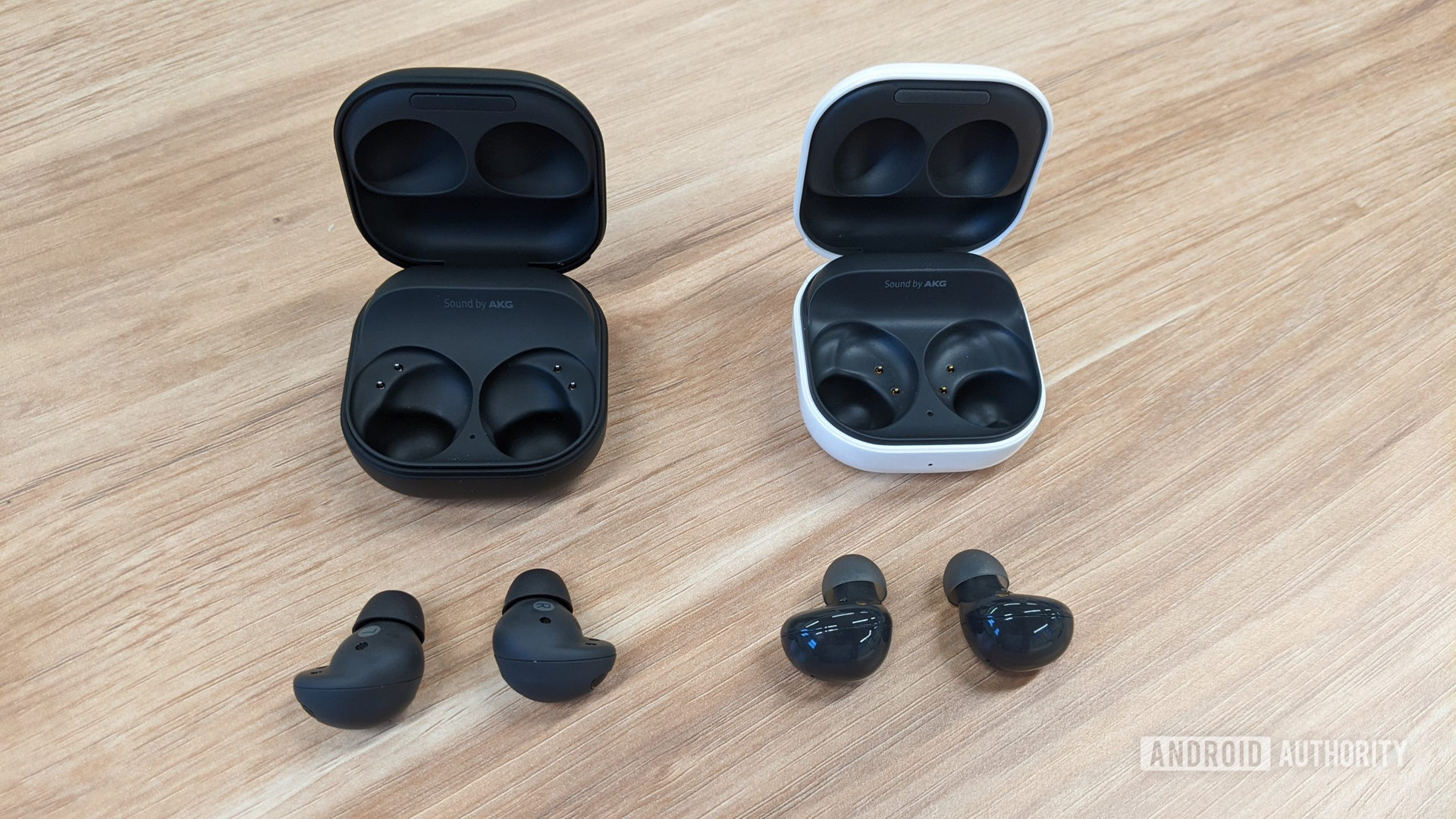 Samsung Galaxy Buds 2 Pro in graphite sitting out of case to the left of Galaxy Buds 2 in graphite out of case (white) on a table.